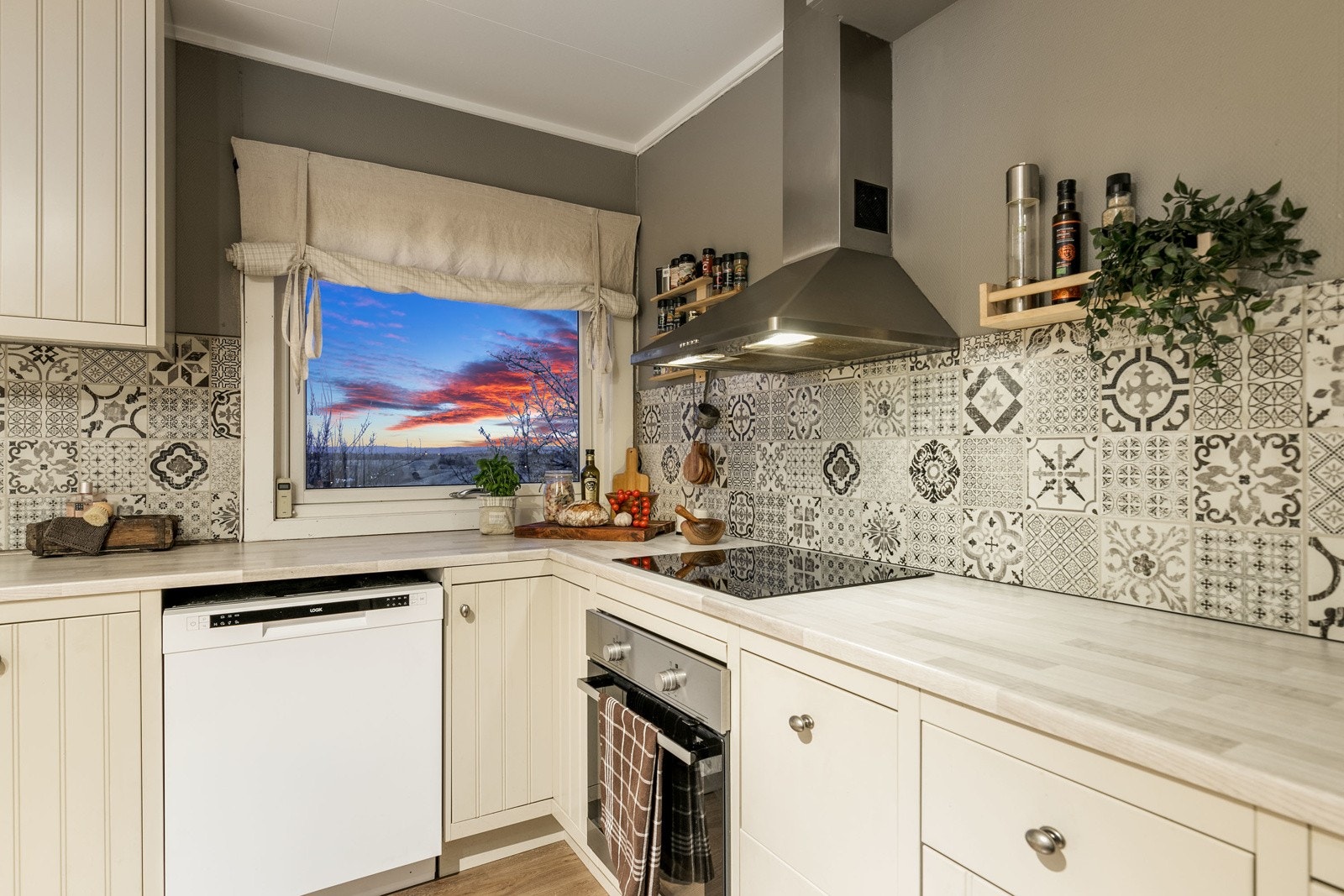 Innredning med kremhvite profilerte fronter i kombinasjon med vitrineskap. Benkeplate av laminat. Nedfelt oppvaskkum med ett-greps kjøkkenarmatur. Galleribilde