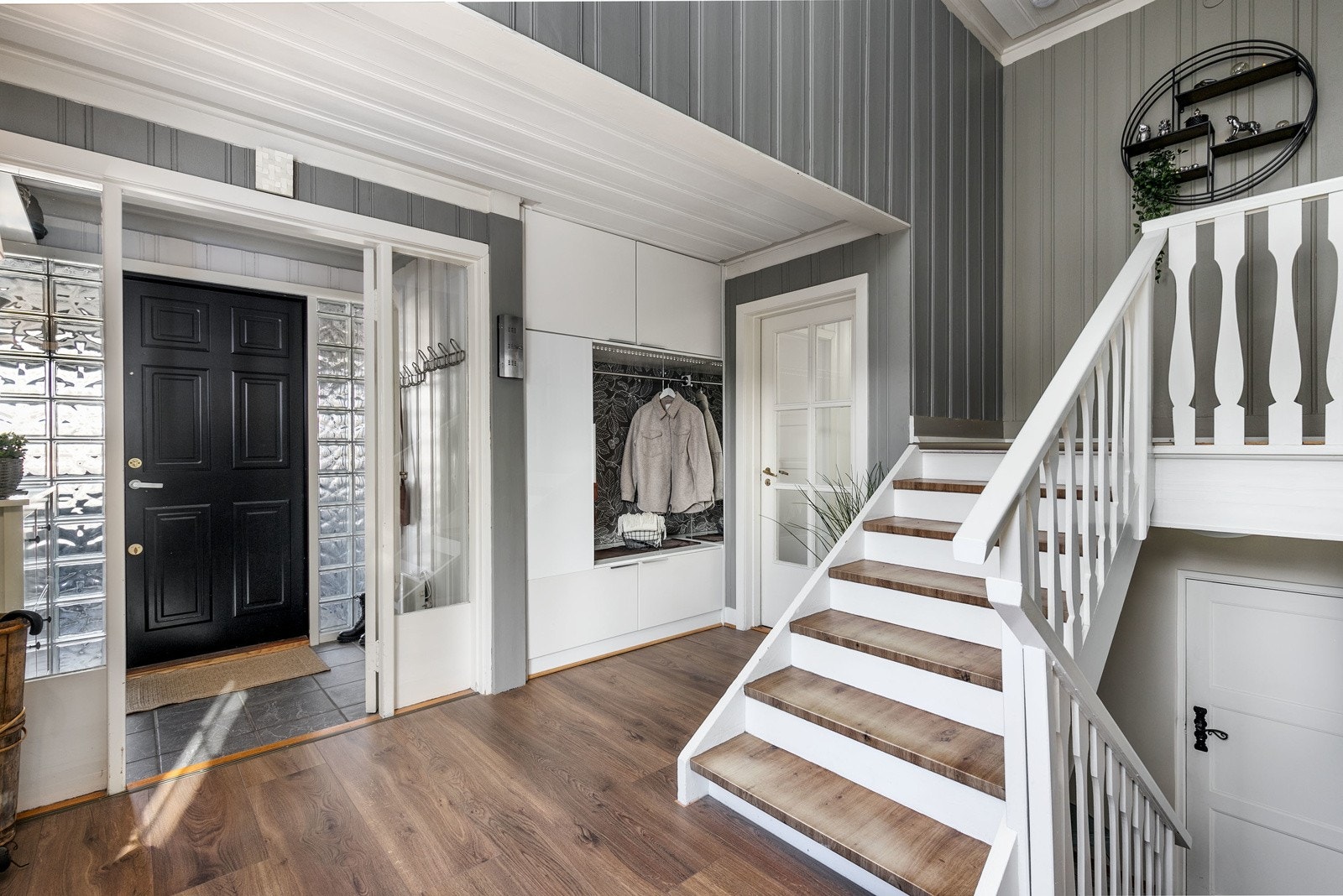 Stor og romslig entre/hall i boligens 2. etasje med fliser på gulv i vindfang. Det er bygget inn en praktisk garderobe like ved inngangspartiet, perfekt til oppbevaring av yttertøy og sko. Galleribilde