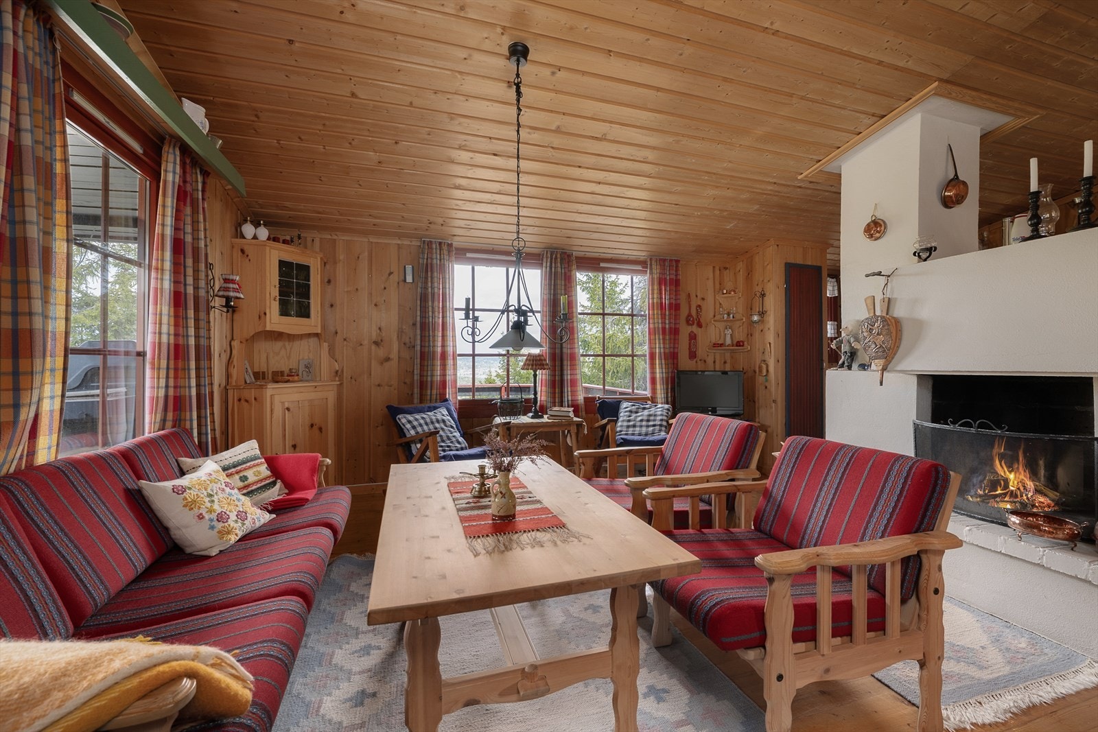 Sofaen er fint plassert foran peisen. Det kommer rikelig med naturlig lys inn i rommet gjennom store vinduer i stua. Galleribilde