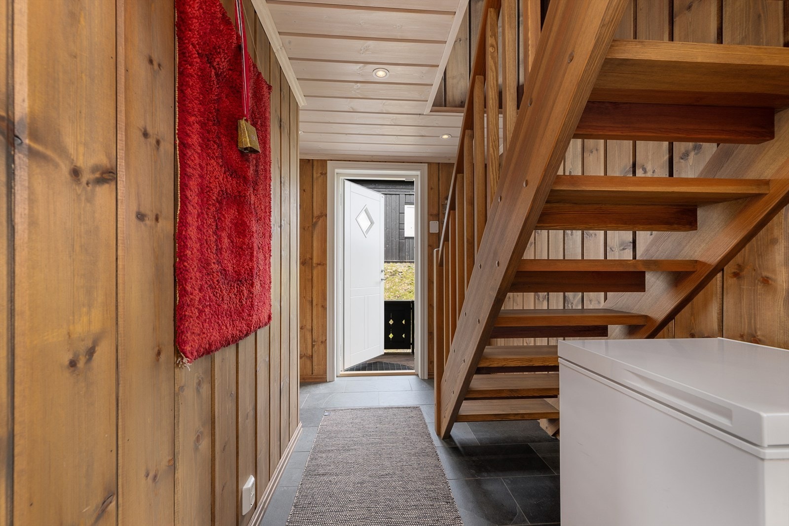 Flislagt gang med trapp opp til hems og adkomst til soverom, bad og inn til oppholdsrommet. Galleribilde