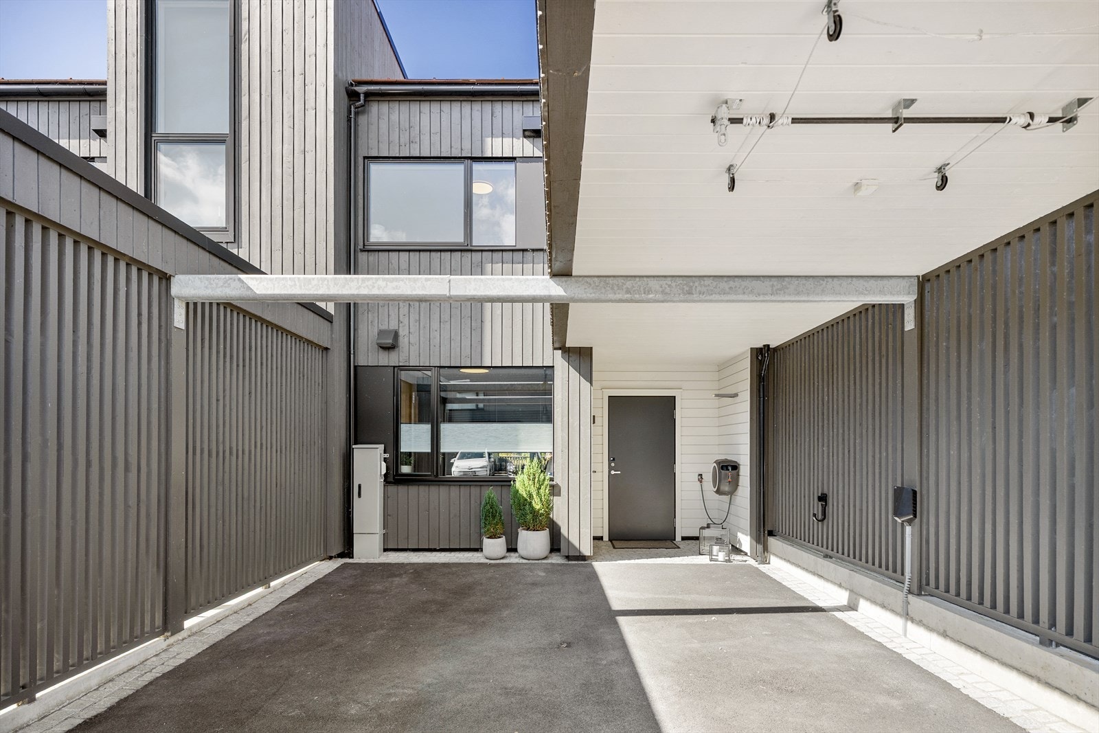 På inngangssiden har boligen en asfaltert carport ombygd i 2024. En lader for elbil er installert, og carporten er en del av et gårdsrom med plass til ytterligere parkering. Galleribilde