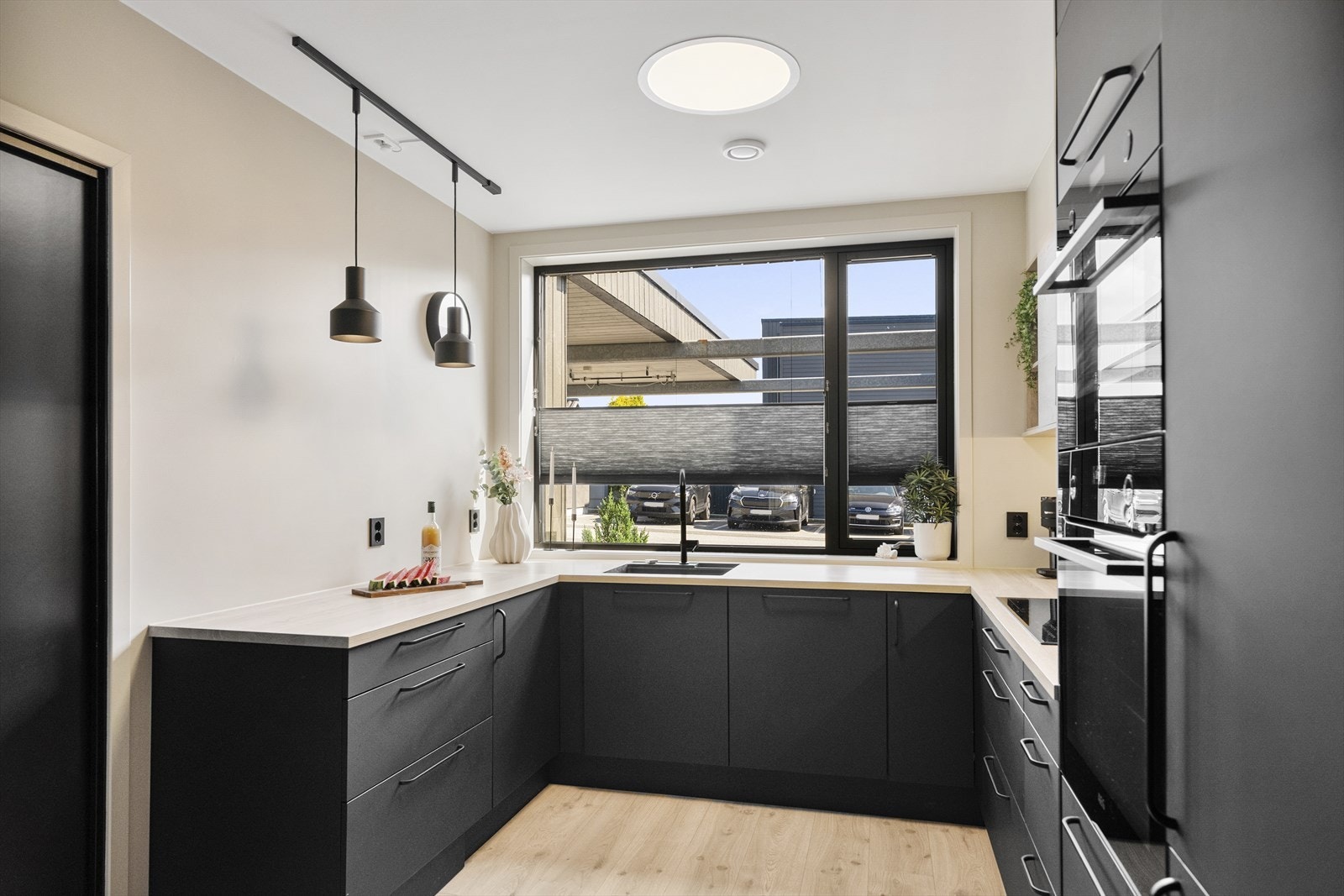 Kjøkkenet er stilrent og moderne, oppført i en smart u-form med god skapplass og fine arbeidsflater. Innredningen har sorte, glatte fronter, laminert benkeplate, nedfelt oppvaskkum i sort utførelse og lyse overskap som matcher benken. Galleribilde