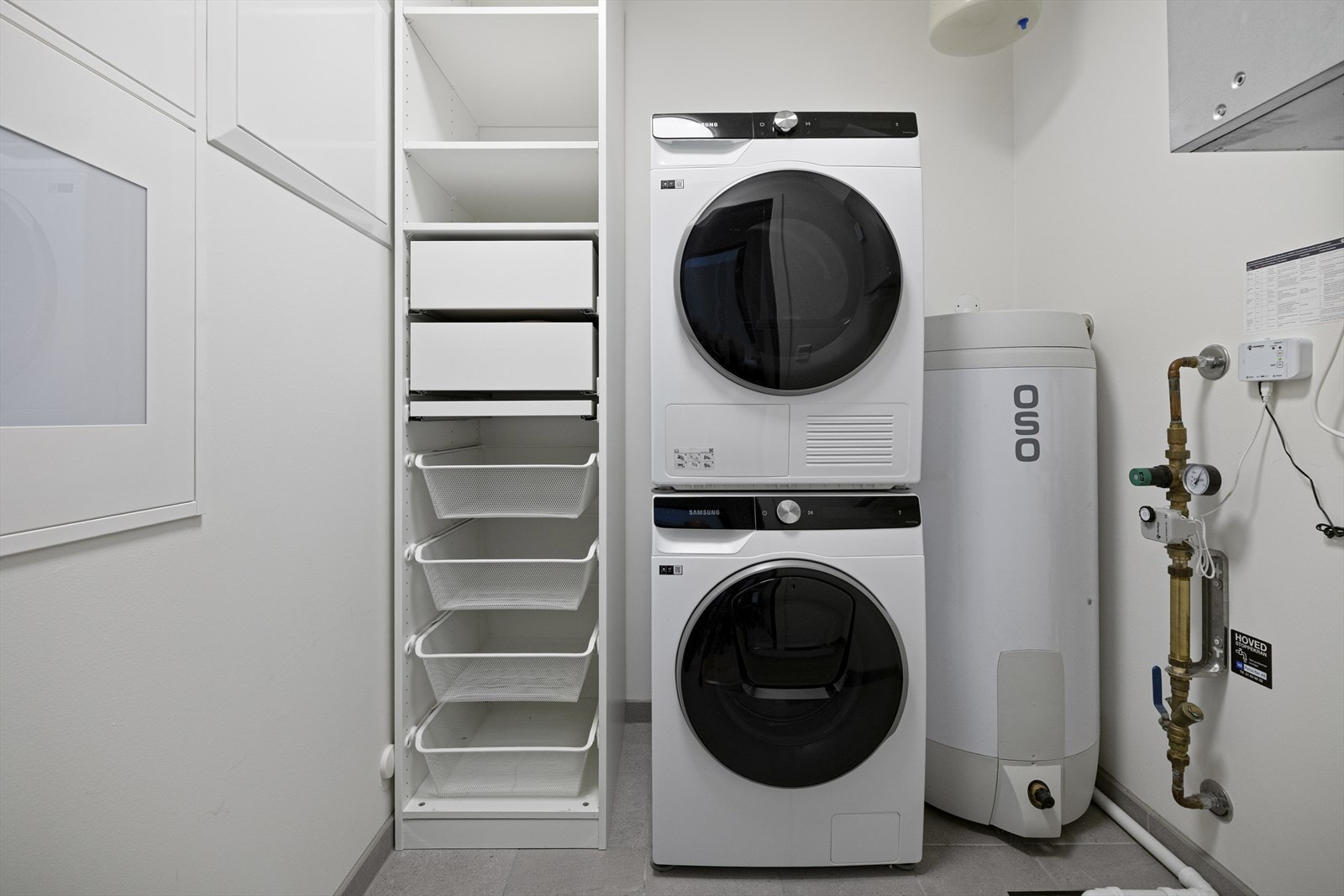 Utenom opplegg for vaskemaskin, har vaskerommet åpne hyller og grå gulvfliser med varme. Galleribilde