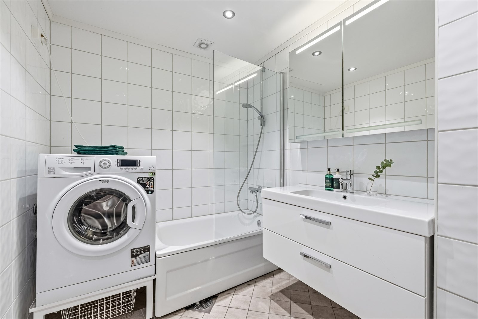 Romslig, flislagt baderom i kjeller med badekar, dusjløsning og opplegg for vaskemaskin. Galleribilde