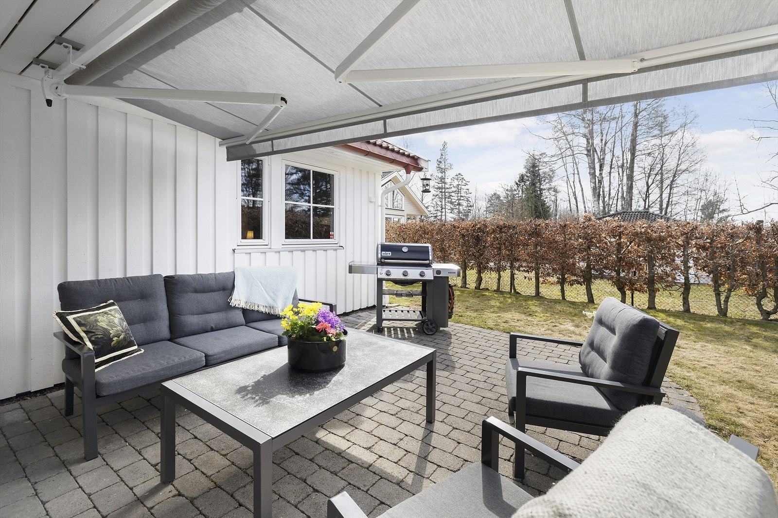 Lun og god uteplass med rom for hagemøbler og grill. Hagen er opparbeidet og enkel å vedlikeholde med muligheter. Hekken rammer inn og skjermer tomten. Markisen er montert i 2023. Galleribilde