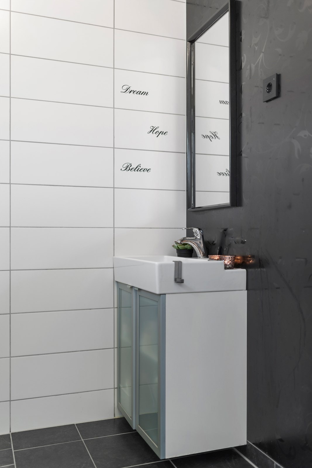 Enkel innredning med vegghengt skap med ovenpåliggende servant og speil, samt stikkontakt Galleribilde