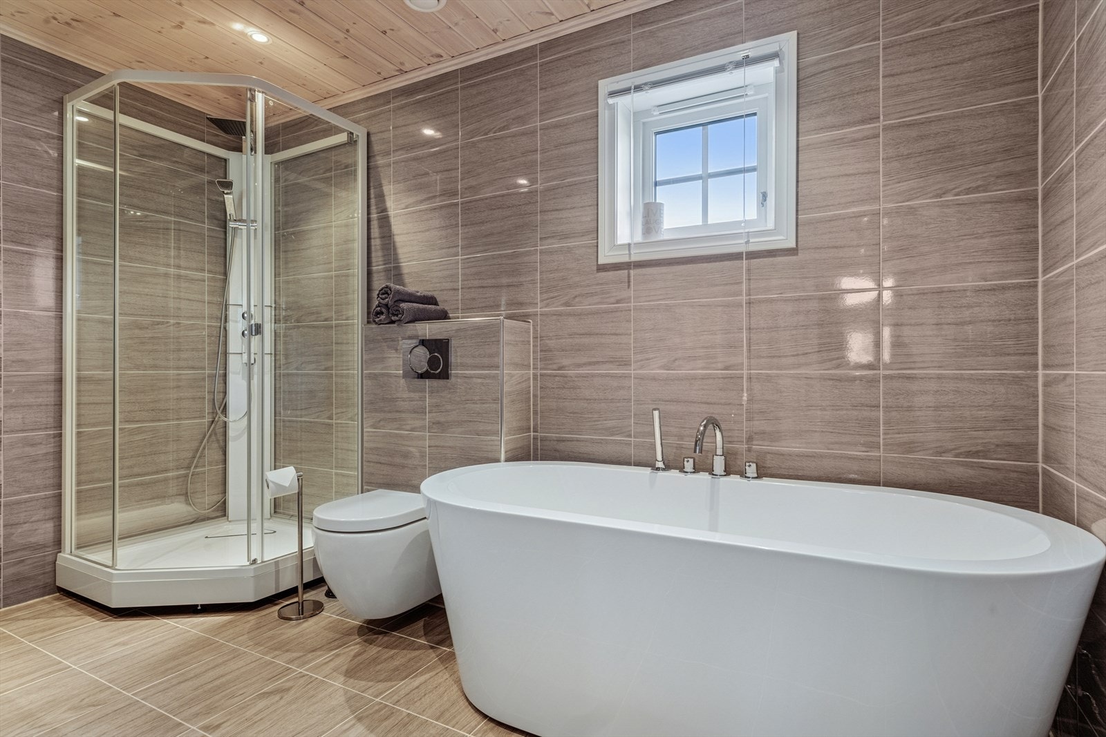 Badet er flislagt med vegghengt toalett, baderomsinnredning med vask, dusjkabinett og badekar. Varmekabler. Galleribilde