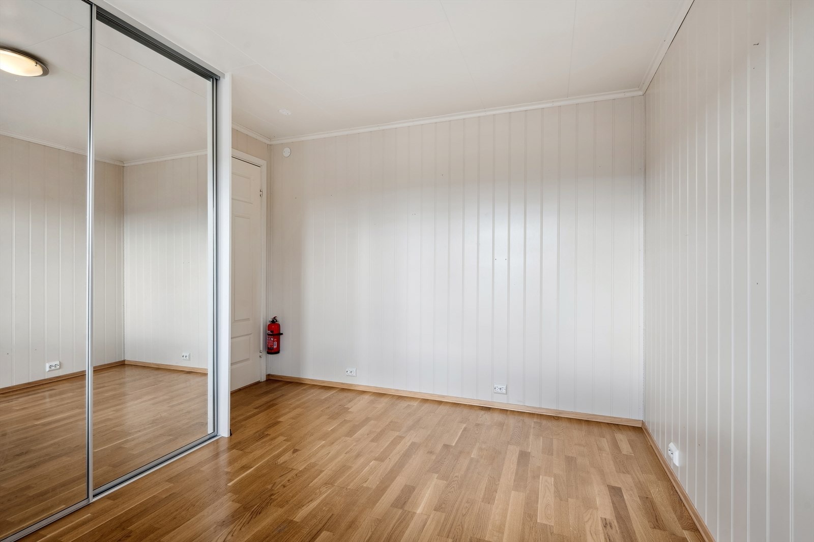 Lyst og romslig soverom med hvite vegger, gjennomgående laminatgulv og en stor skyvedørsgarderobe med speil. Galleribilde