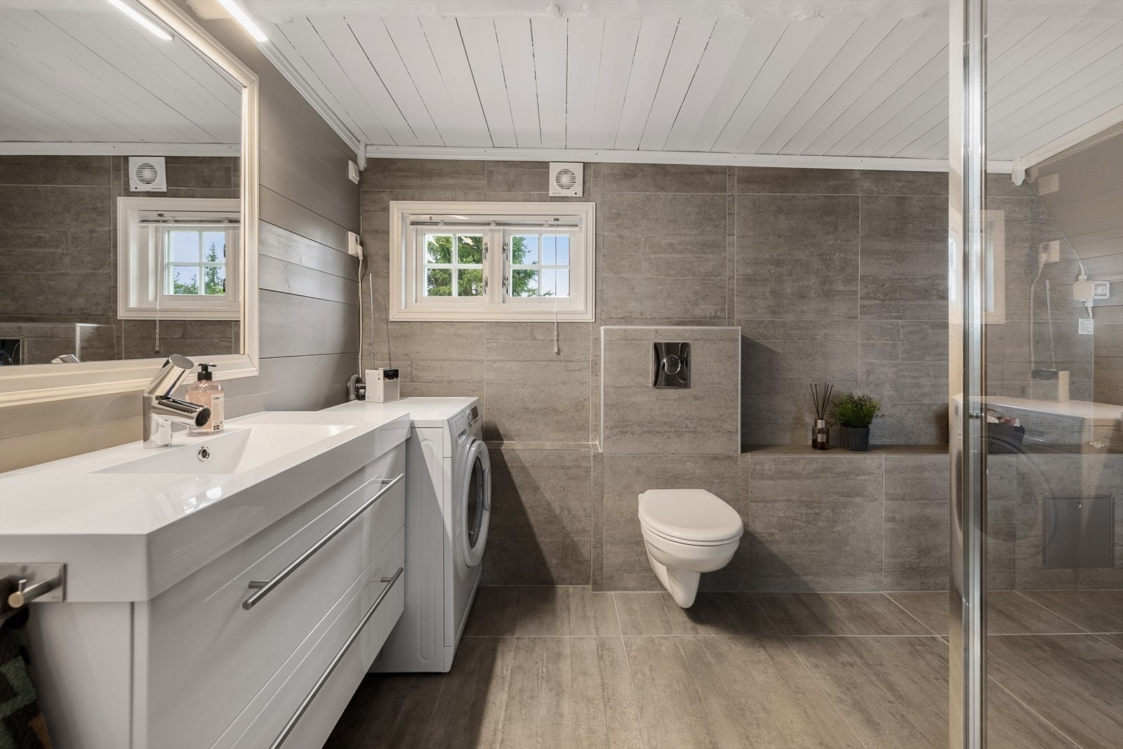 Meget pent, flislagt bad/wc med dusj, vegghengt WC, servantinnredning og opplegg for vaskemaskin. Galleribilde