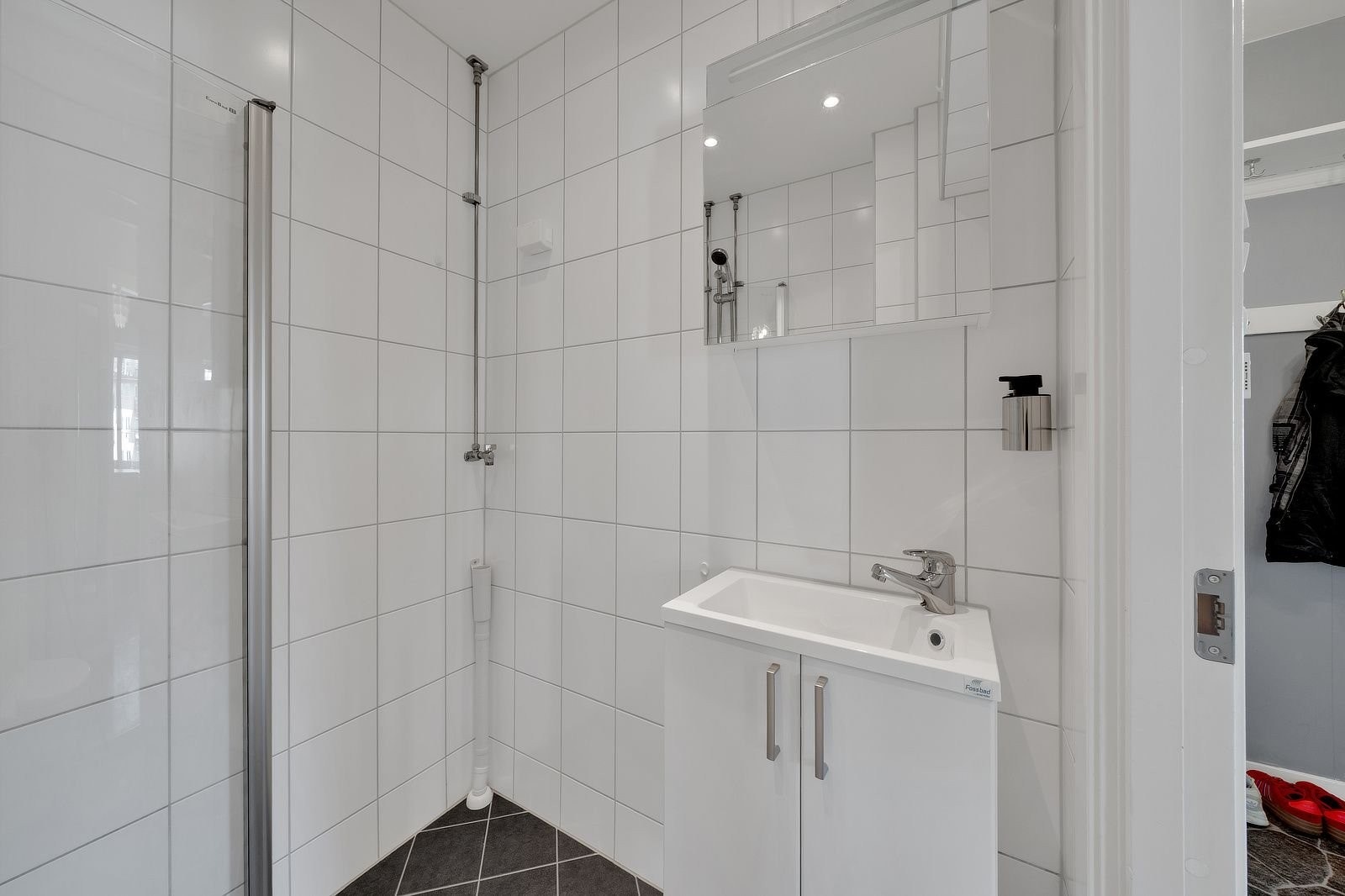 Badet er innredet med vegghengt toalett, dusjhjørne med dusjdører, servant med skap og opplegg for vaskemaskin. Galleribilde