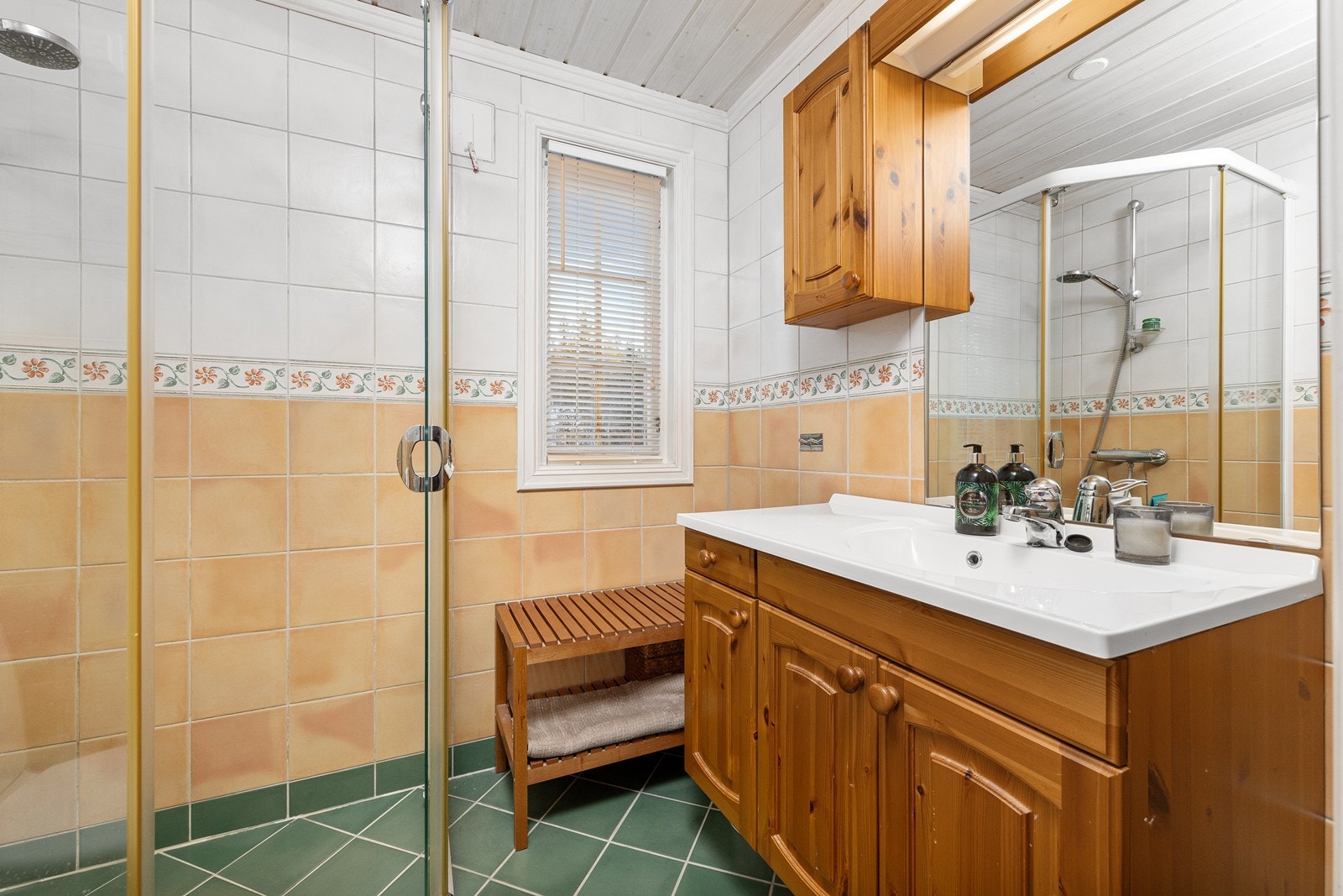 Baderommet er flislagt og har elektrisk gulvvarme for en komfortabel opplevelse. Det er innredet med en praktisk baderomsmøbel med nedfelt servant, toalett og dusjvegger i hjørneløsning. Galleribilde