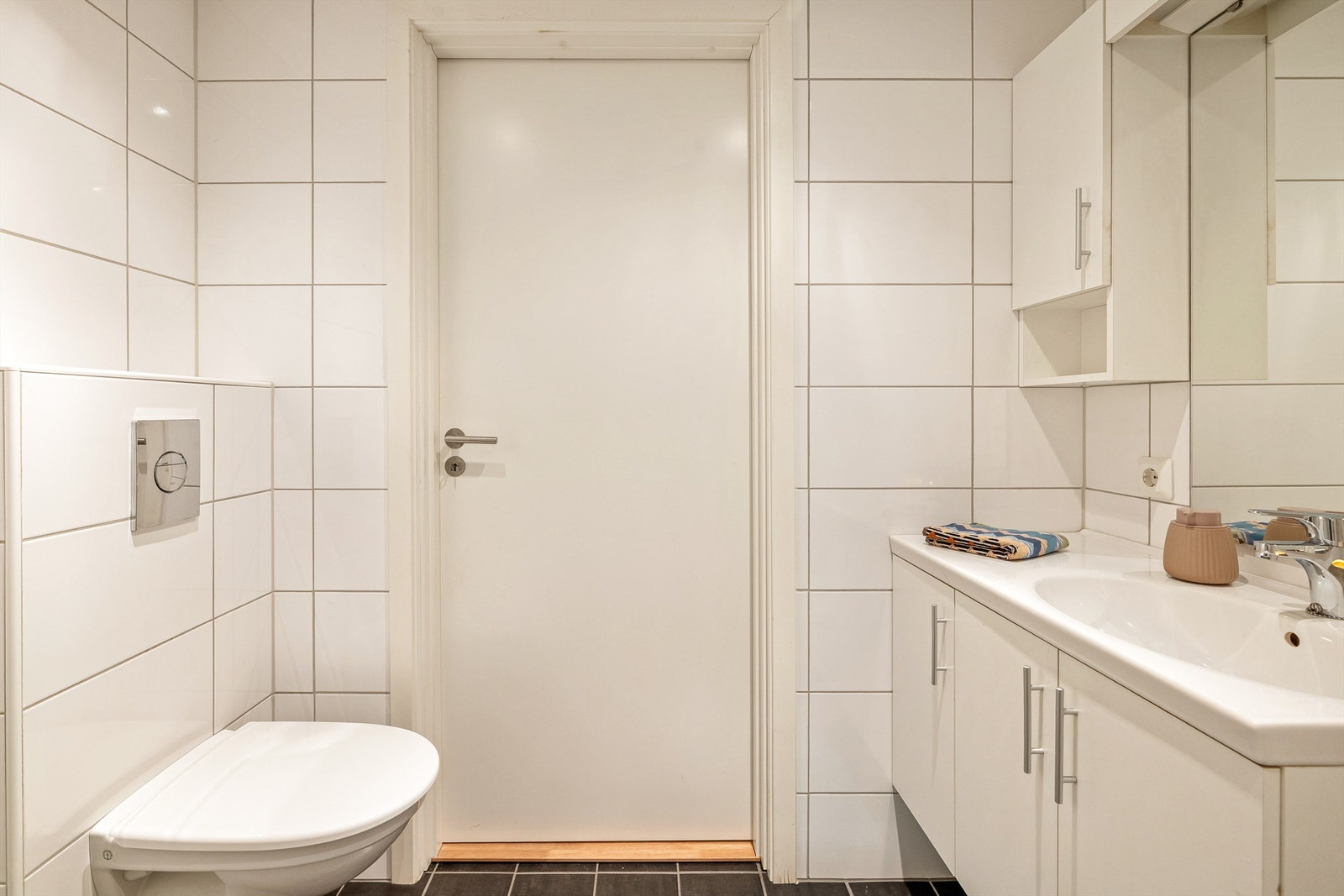 Fliser med tidløse fargevalg, dusj med innvendbare glassdører og veggmontert toalett Galleribilde