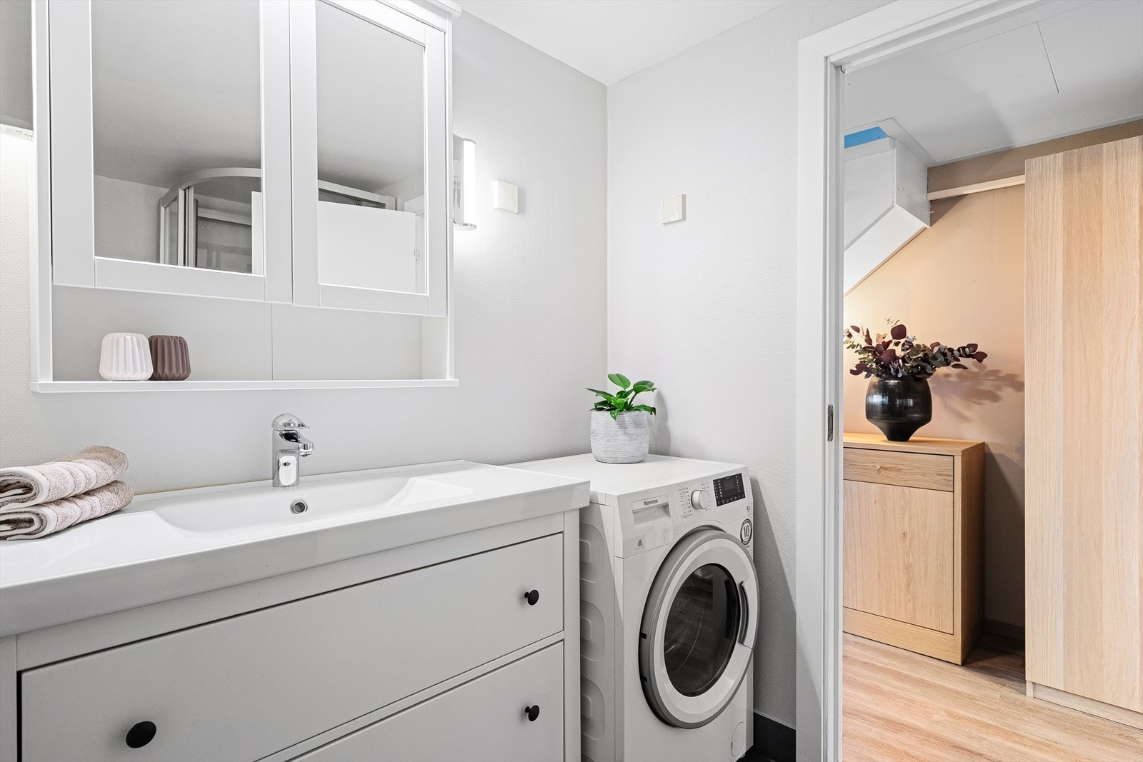 Her er det innredet med hvit baderomsinnredning, grå gulvfliser med varmekabler og lys våtromstapet på veggene. Heldekkende servant med god oppbevaringsplass og speilskap på veggen, dusjkabinett og opplegg for vaskemaskin. Galleribilde