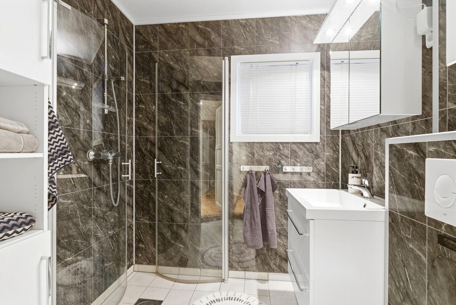 Bad med baderomsplater på veggene og flislagt gulv med varme. Badet har moderne innredning, veggmontert toalett og dusjhjørne. Galleribilde