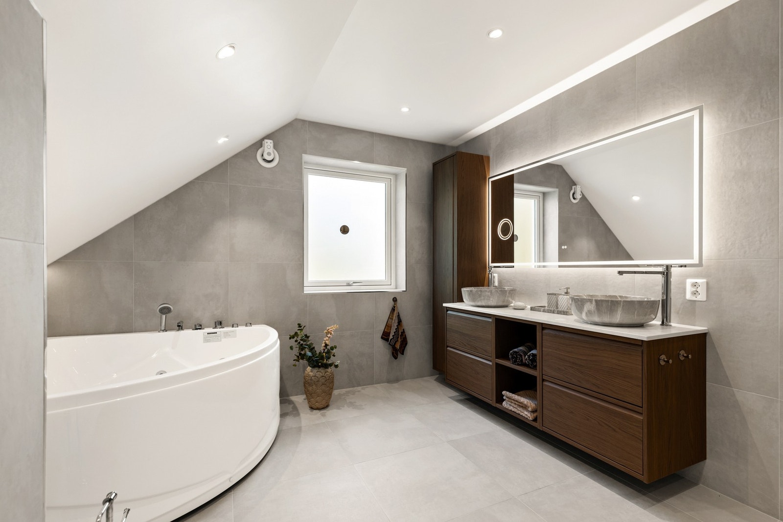 På en mørk skuffeinnredning er det to toppmonterte, runde servanter, og over er det et stort speil med belysning. Galleribilde