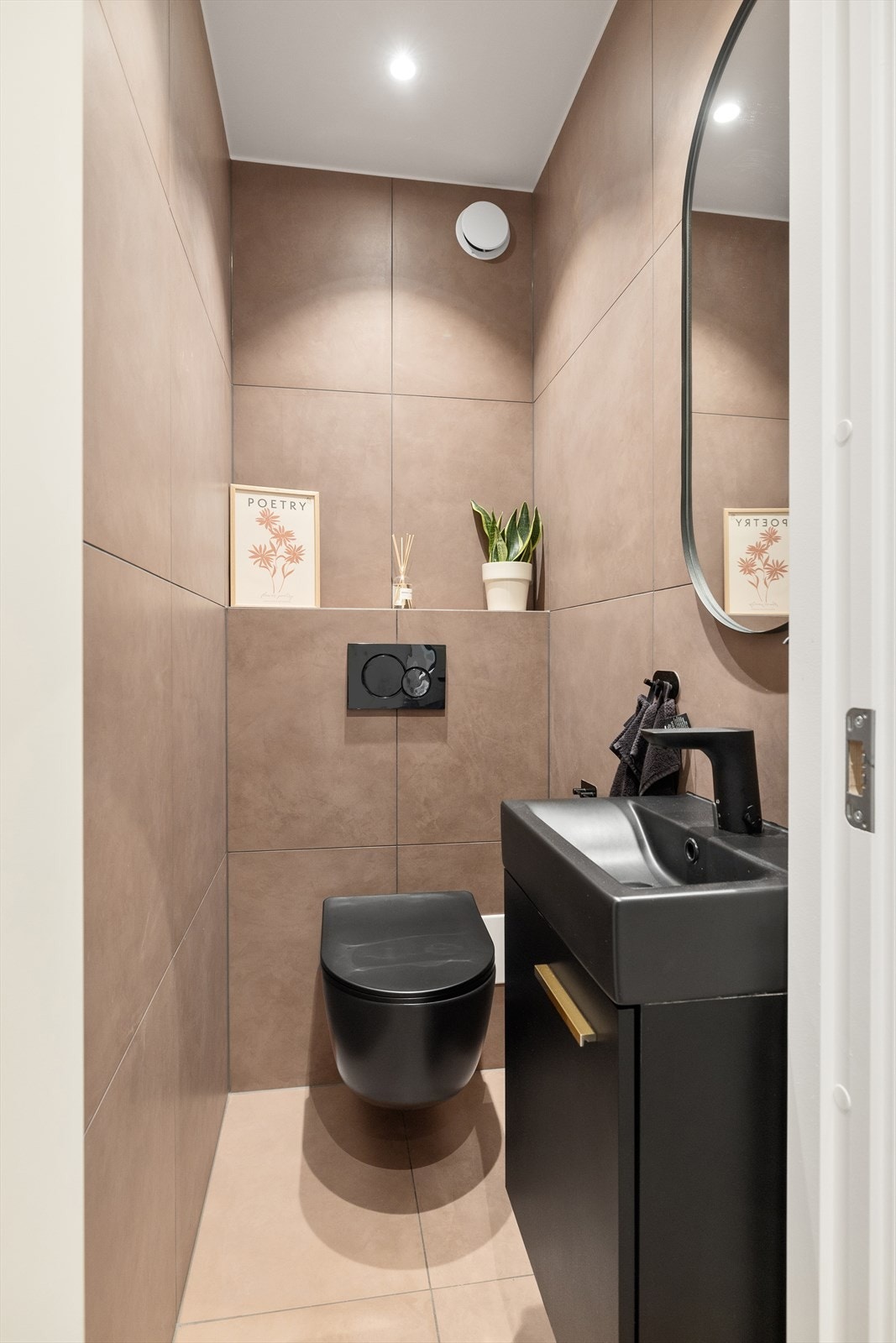 Vegg i vegg med baderom ligger et praktisk toalettrom, innredet med vegghengt servantskap med glatt front og heldekkende servant med ett-greps armatur, speil over servant, og vegghengt toalett. Galleribilde