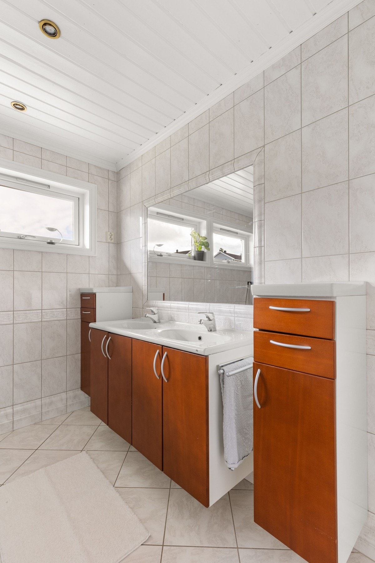 Romslig baderom med gulvvarme og fliser på både gulv og vegger. Lyse flater kombinert med innfelte downlights i tak. Galleribilde