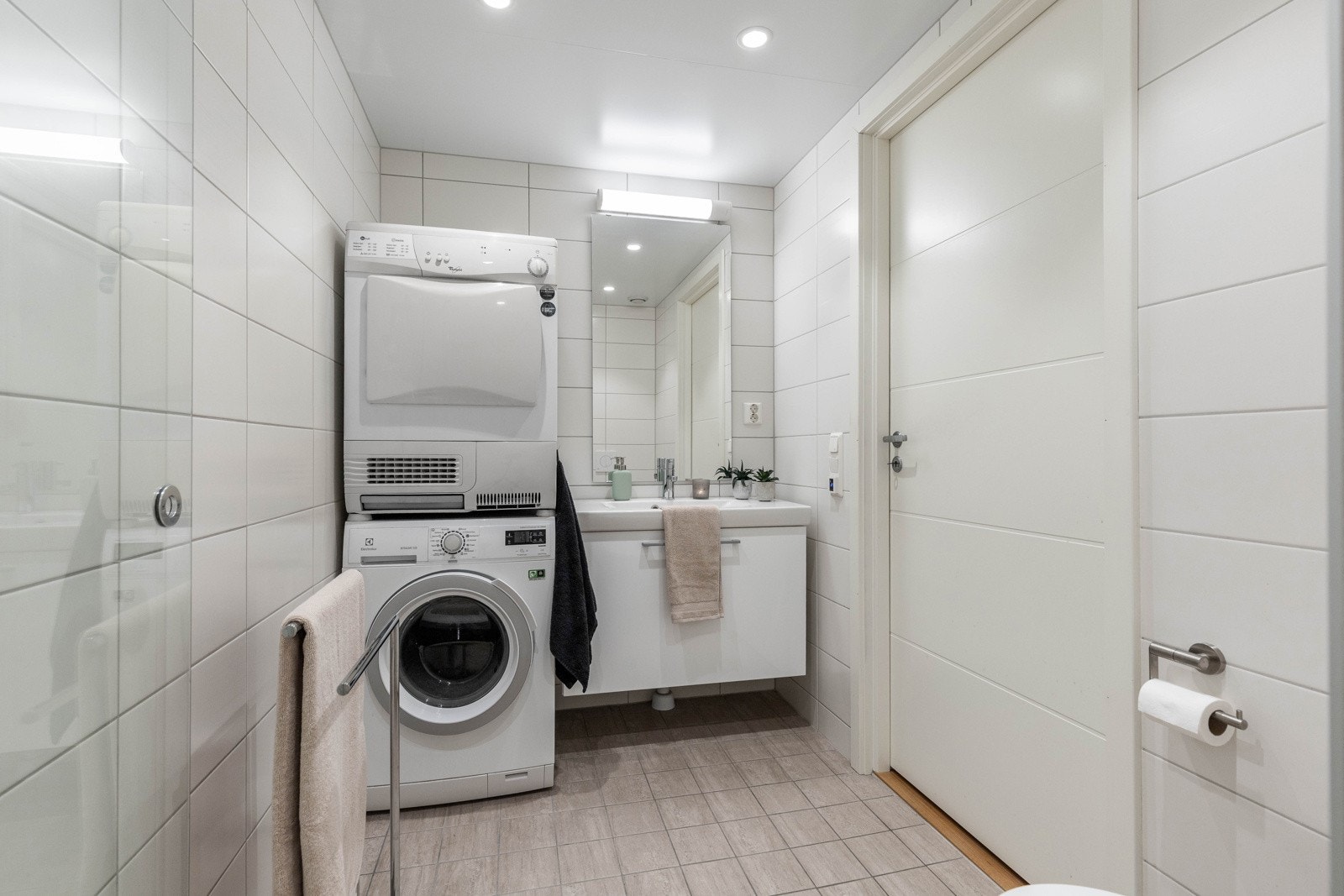 Stilrent bad med fliser på både gulv og vegger, god belysning og plass til både vaskemaskin og tørketrommel. Galleribilde