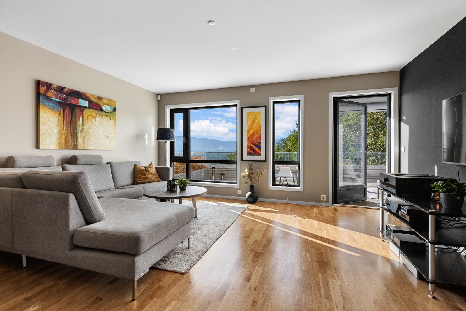 Store vindusflater slipper inn rikelig med naturlig lys og skaper en luftig atmosfære. Stuen binder inne og ute sømløst sammen. Ideelt for lyse sommerdager. Galleribilde