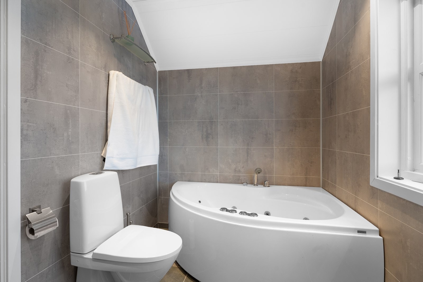 Badet inneholder toalett, badekar og innredning med dobbel servant Galleribilde