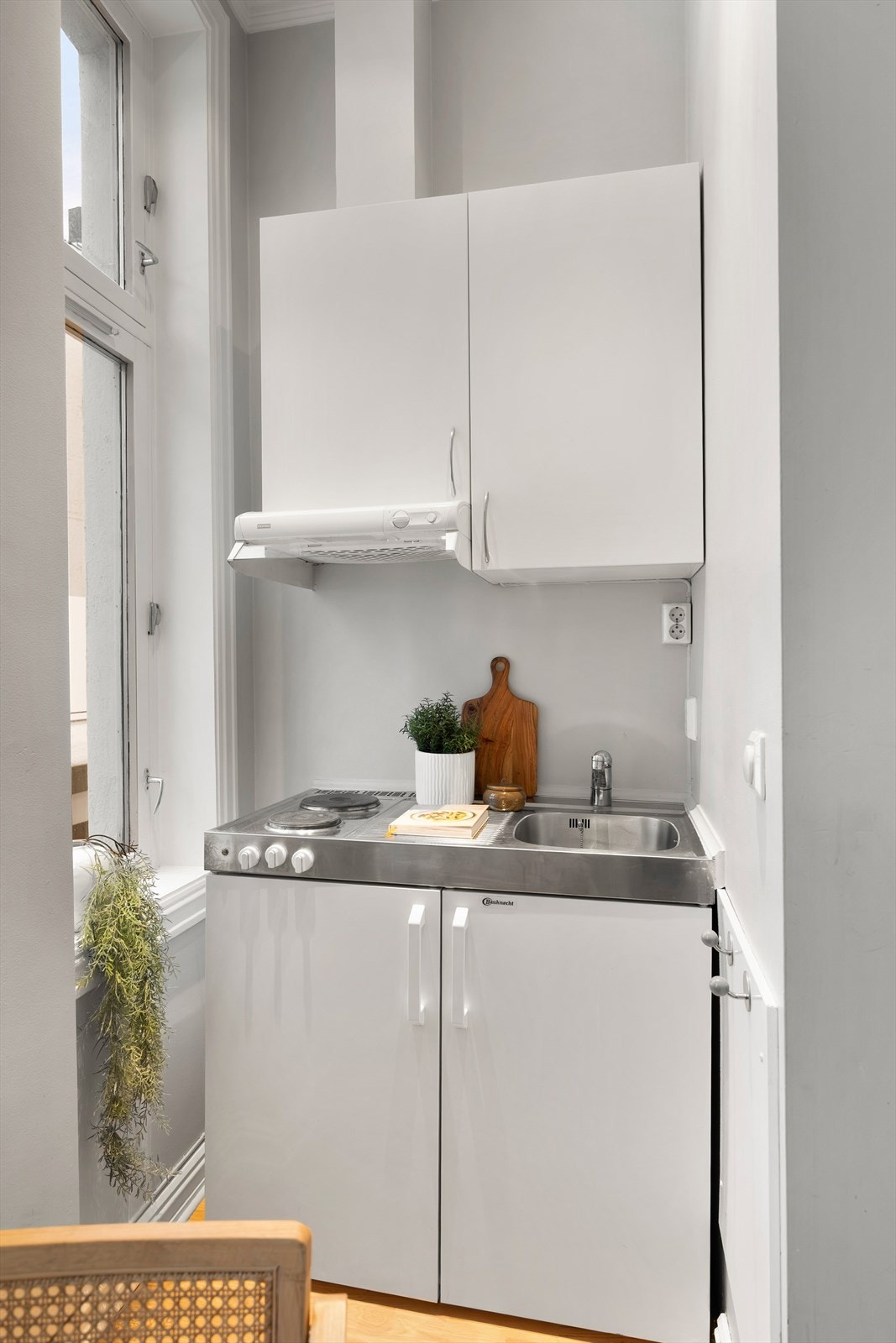 Hybelkjøkken med glatte fronter og praktisk utforming. Benkeplate i stål med kokeplater og oppvaskkum med ettgreps armatur fra FM Mattsson. Det er integrert kjøleskap. Galleribilde