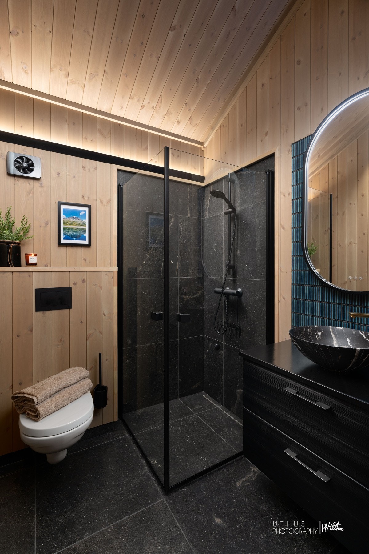 Badene har 60x60 fliser på gulv og i dusjhjørne fra Modena og av typen Ibla Nera Lappato (Ibla er en gjenskapning av en fantastisk flott mørk og sofistikert kalkstein med innhold av fossile hydrokarboner (olje/asfaltstein) fra den sicilianske byen Ragusa. Galleribilde