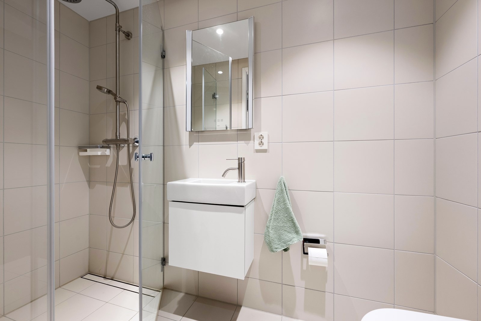 Lekkert bad med adkomst fra entreen - Badet er videre innredet med veggmontert toalett, servant, dusjhjørne og glatt servantskap Galleribilde