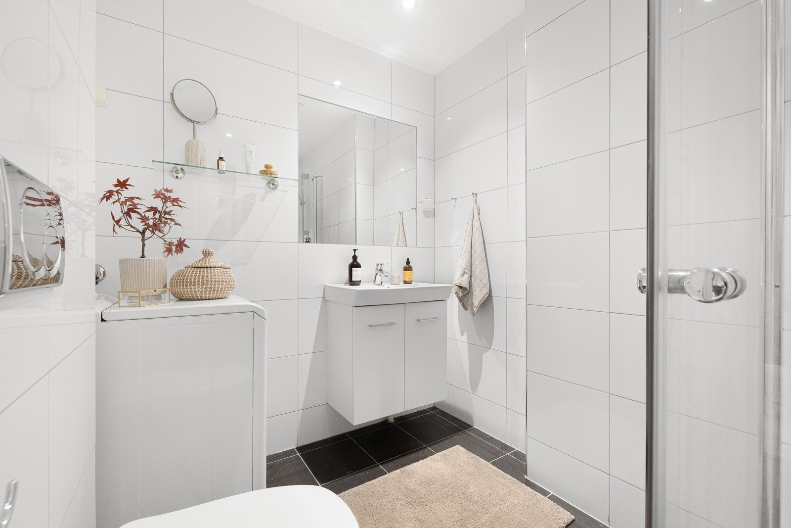 Badet er utstyr med opplegg for vaskemaskin, veggmontert toalett og dusjhjørne med glassdører og ettgreps krummet dusjarmatur. Galleribilde