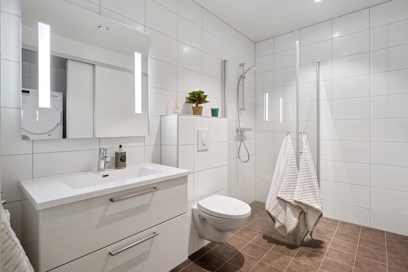 Moderne, helfliset bad med vegghengt toalett, dusjhjørne og servantinnredning. Galleribilde