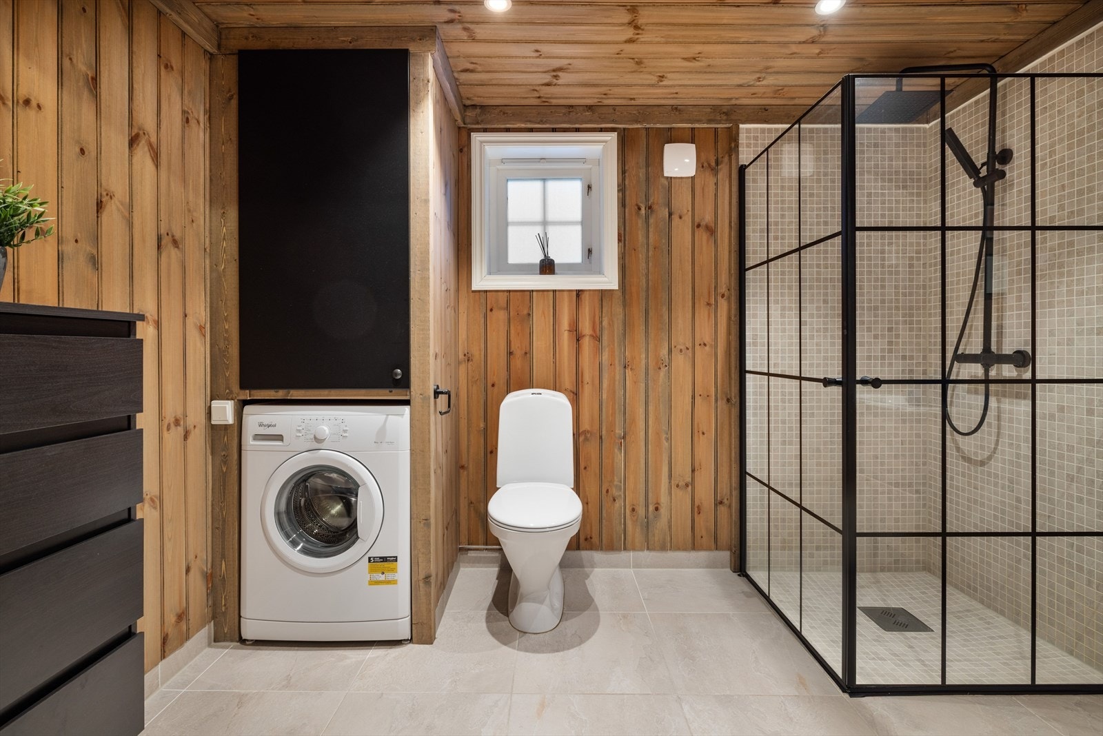 Hytta har et flott baderom fra byggeåret 2020. Baderommet har grå fliser på gulv med gulvvarme, trepanel på veggene kombinert med fliser i dusjsonen, downlights i himlingen og elektrisk baderomsvifte. Galleribilde