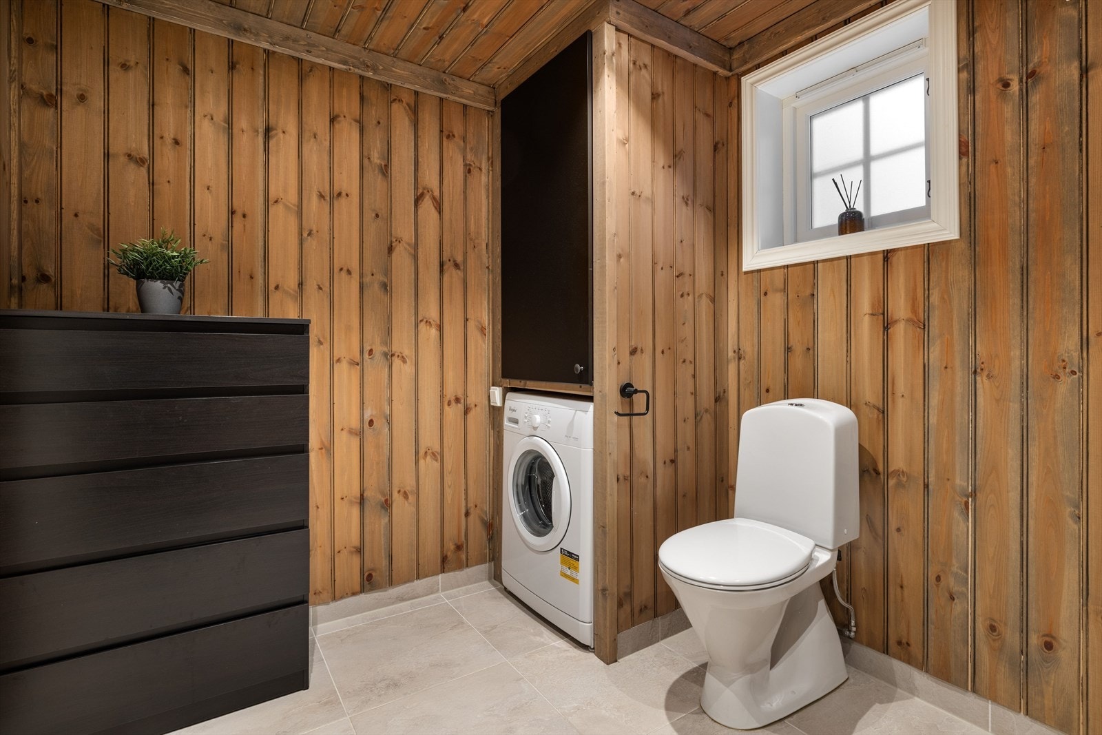 Baderommet er også utstyrt med gulvstående toalett. Praktisk nisje med plass og opplegg for vaskemaskin og skap med varmtvannsbereder over. Galleribilde