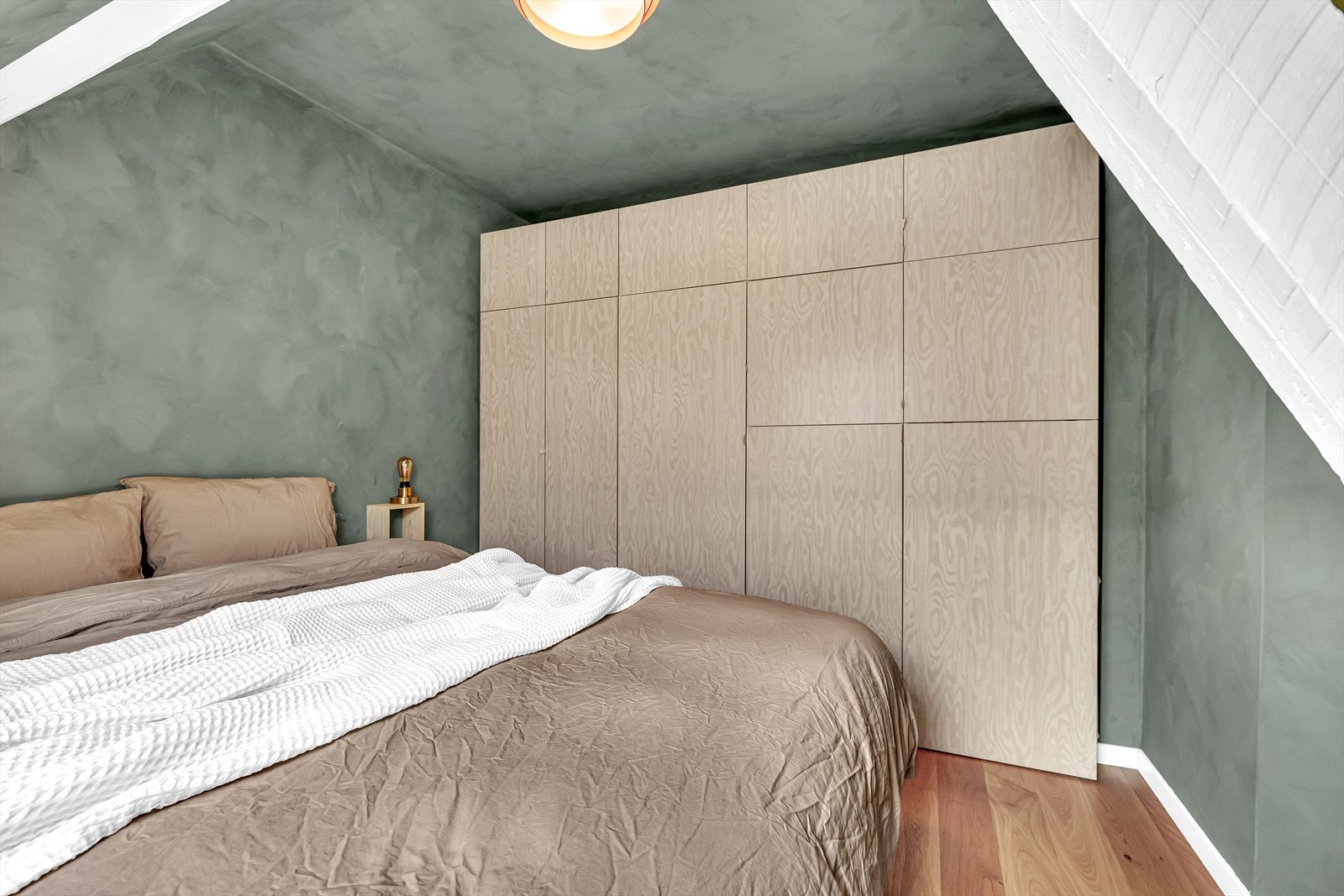 Innebygd garderobe gir rikelig med oppbevaringsplass og et ryddig helhetsinntrykk. Malte vegger i dus grønnfarge bidrar til et lunt og avdempet sovemiljø. Galleribilde