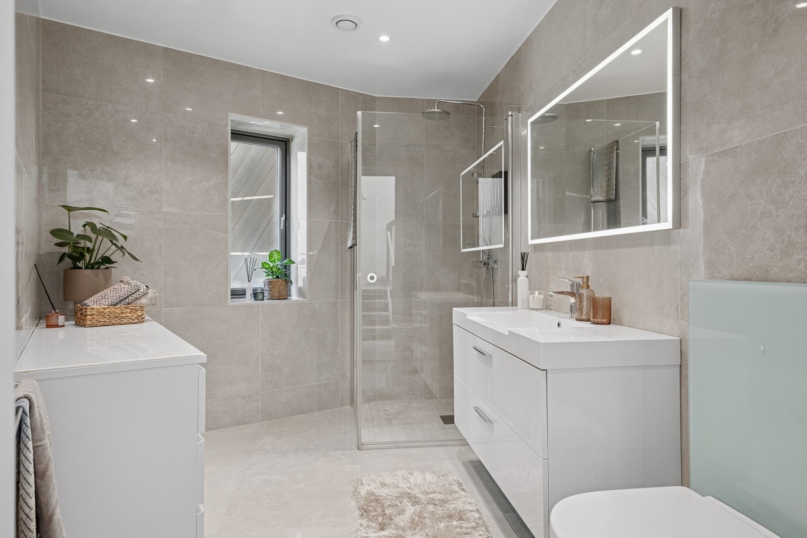 Ett av boligens to store bad. Badet er i delikat utførelse med lyse fliser (60*60 cm ) med varme i gulv. Praktisk dusjhjørne (100*100 cm) med innfellbare dører. Innfelte downlights i tak. Galleribilde