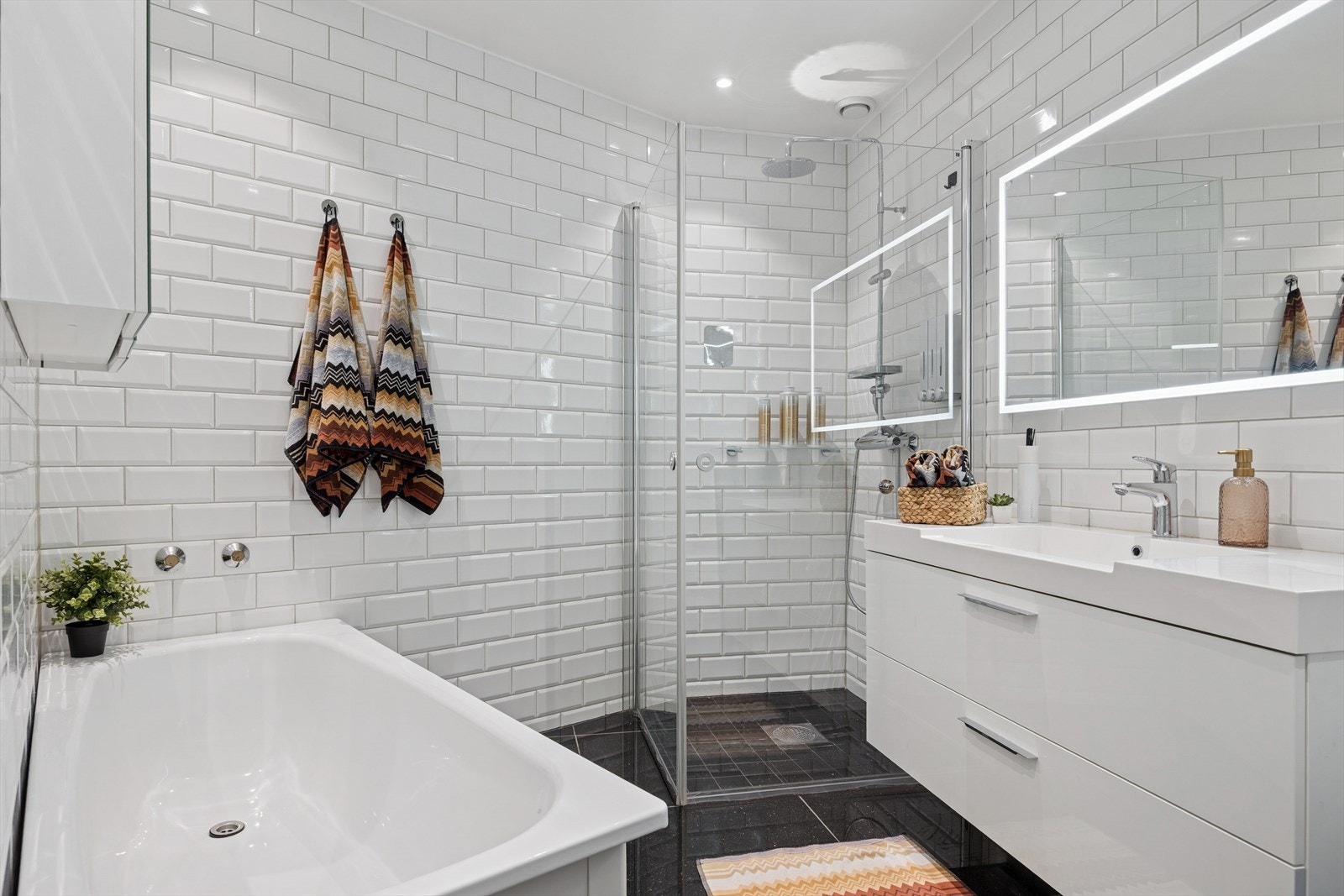 Pent flislagt bad utstyrt med skuffeinnredning med overliggende servant, dusj med innfellbare glassvegger og dusjgarnityr på vegg, vegghengt toalett og badekar. Galleribilde