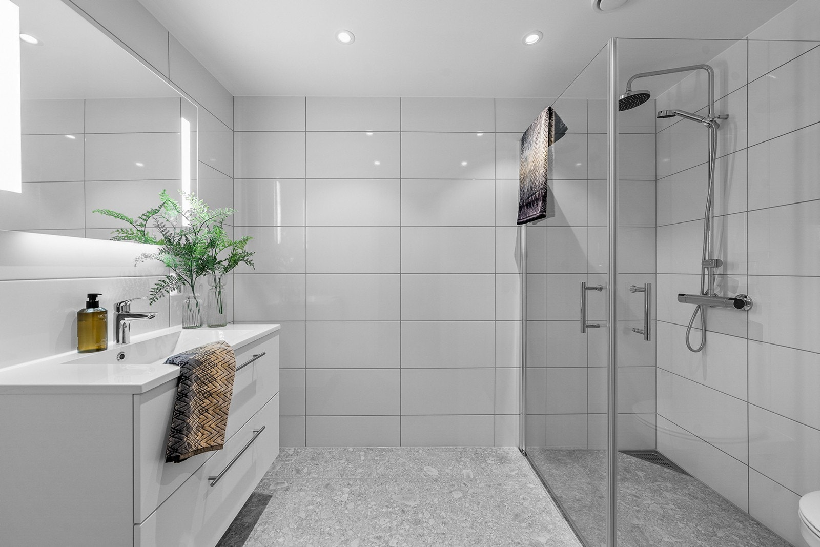 Lekkert og moderne bad med flislagt gulv med elektriske varmekabler og flislagte vegger. Her er det innfelte downlights i himlingen som gir et stilrent og godt belyst rom Galleribilde