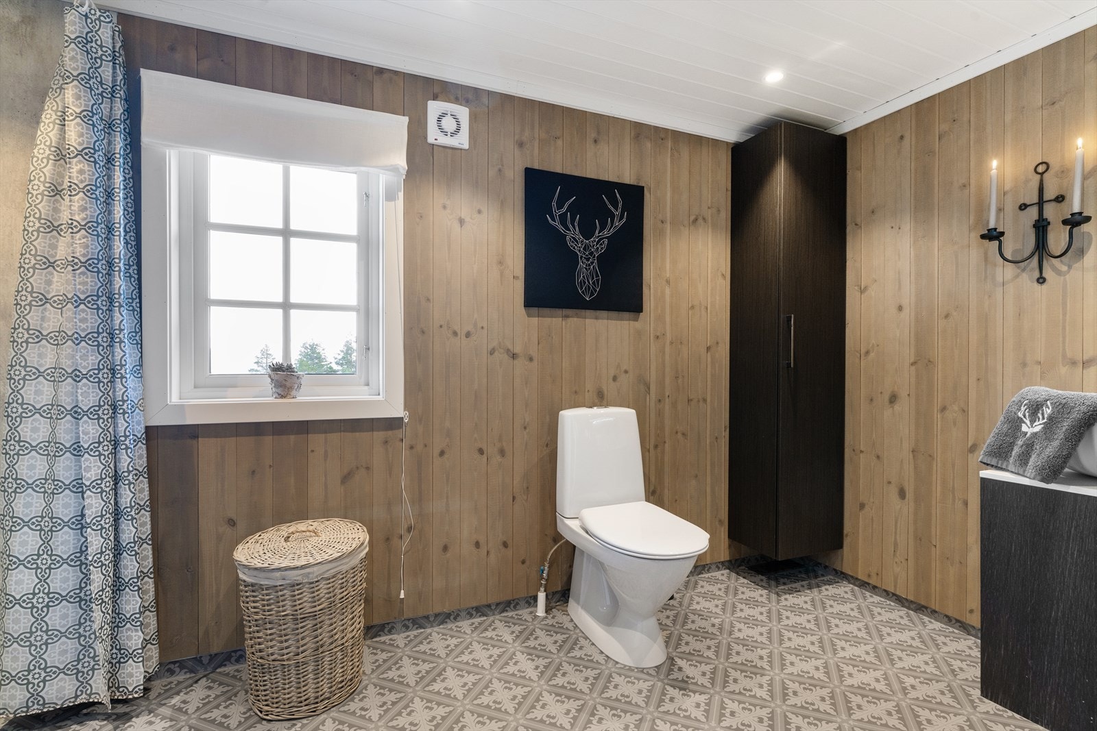 Veggene har en kombinasjon av trepanel og baderomsplater, mens taket er kledd i panel. Gulvet har vinylbelegg med klassisk mønster og elektriske varmekabler som sørger for god komfort. Galleribilde