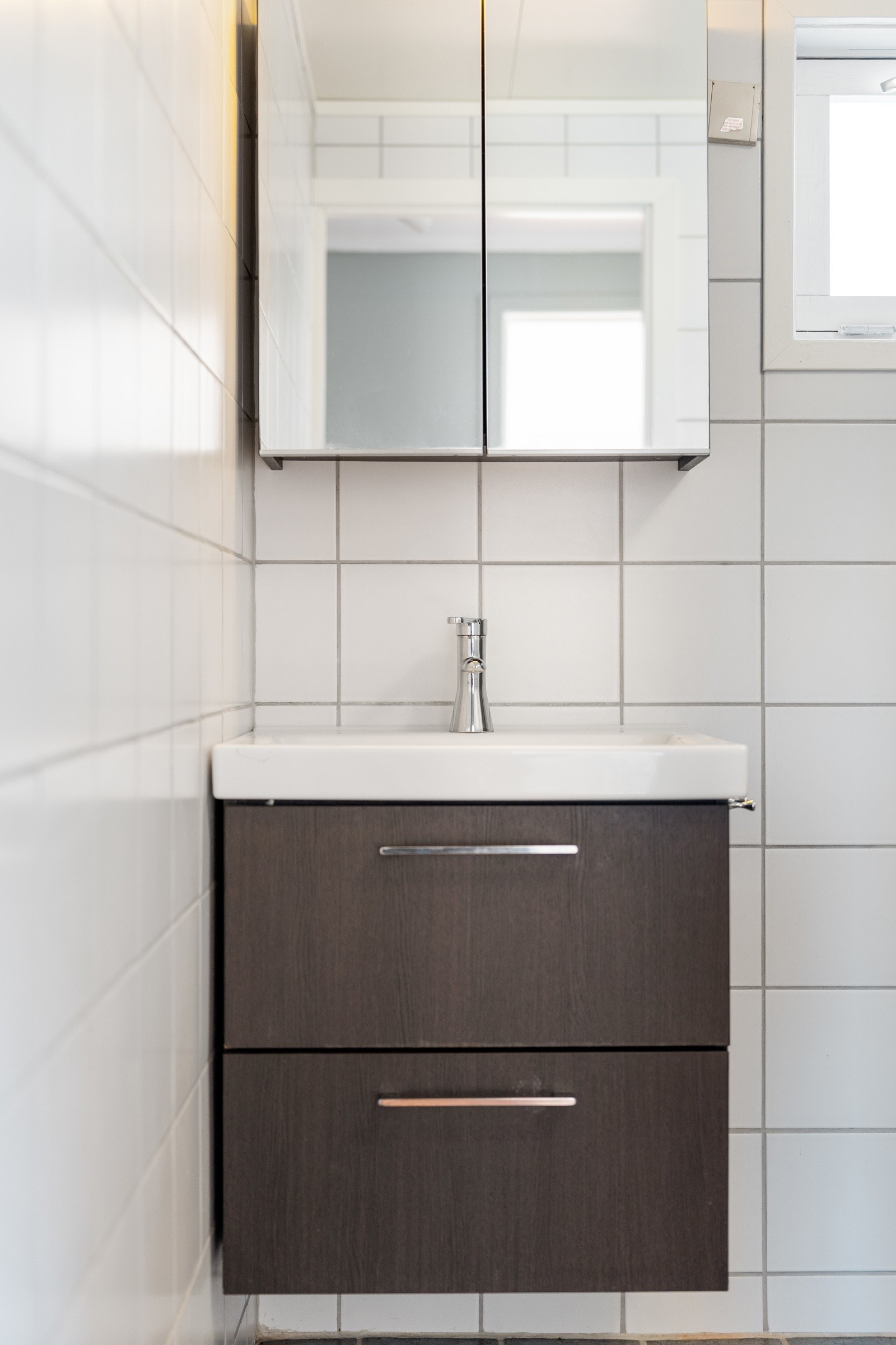 Det er innredet med servant og brunt underskap med skuffer, speil med oppbevaringsmuligheter, dusjkabinett og toalett. Galleribilde