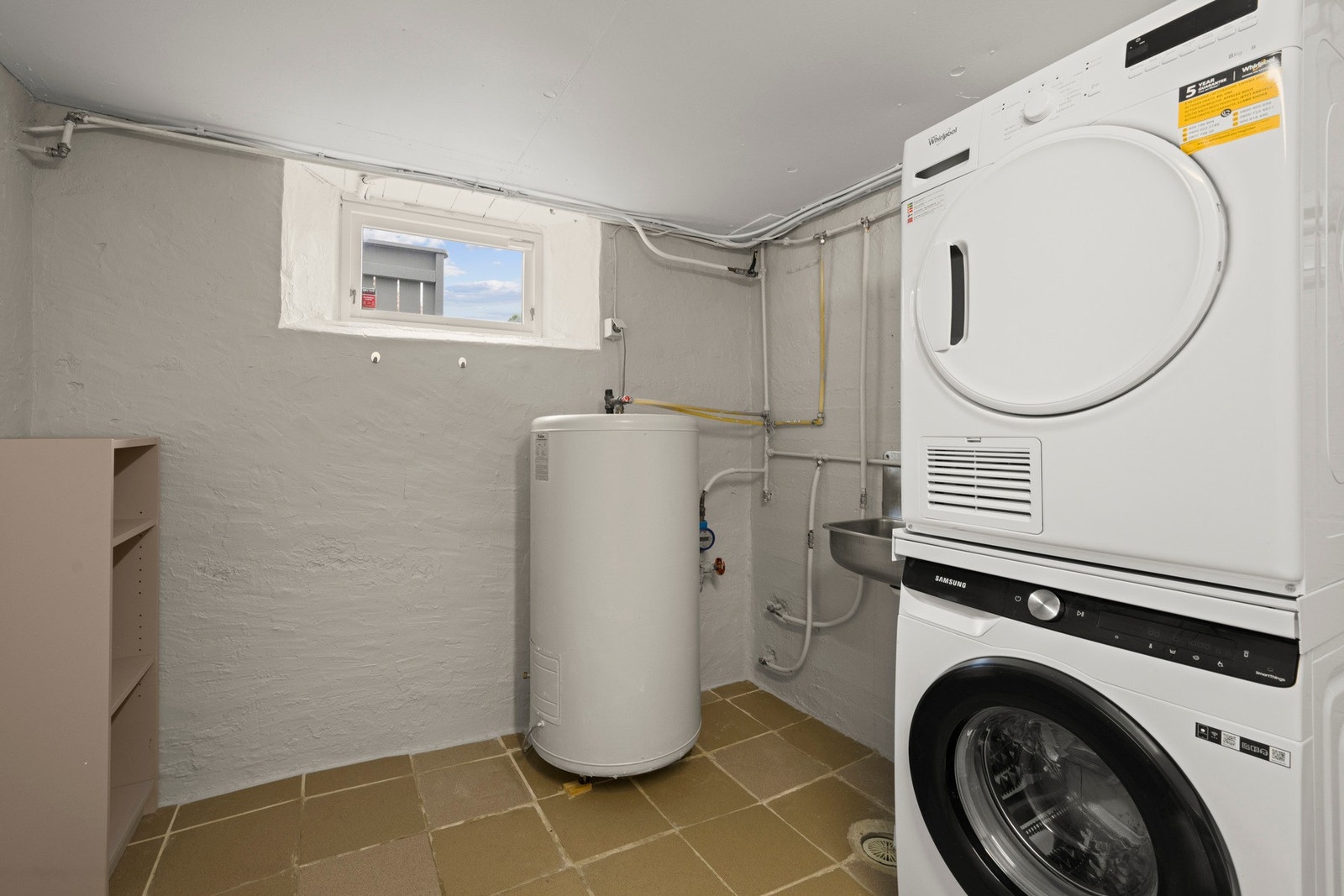 Praktisk vaskerom med fliser på gulv, malte betongvegger og opplegg for vaskemaskin. Galleribilde