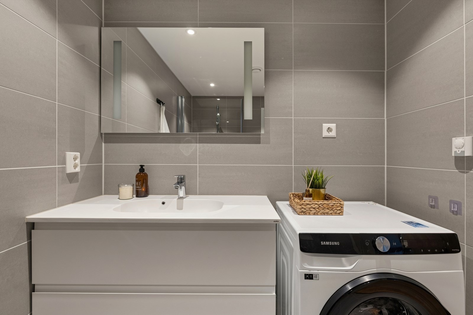 Badet har servant med slette fronter, veggmontert toalett, dusjhjørne med to svingbare glassdører, samt opplegg for vaskemaskin. Galleribilde