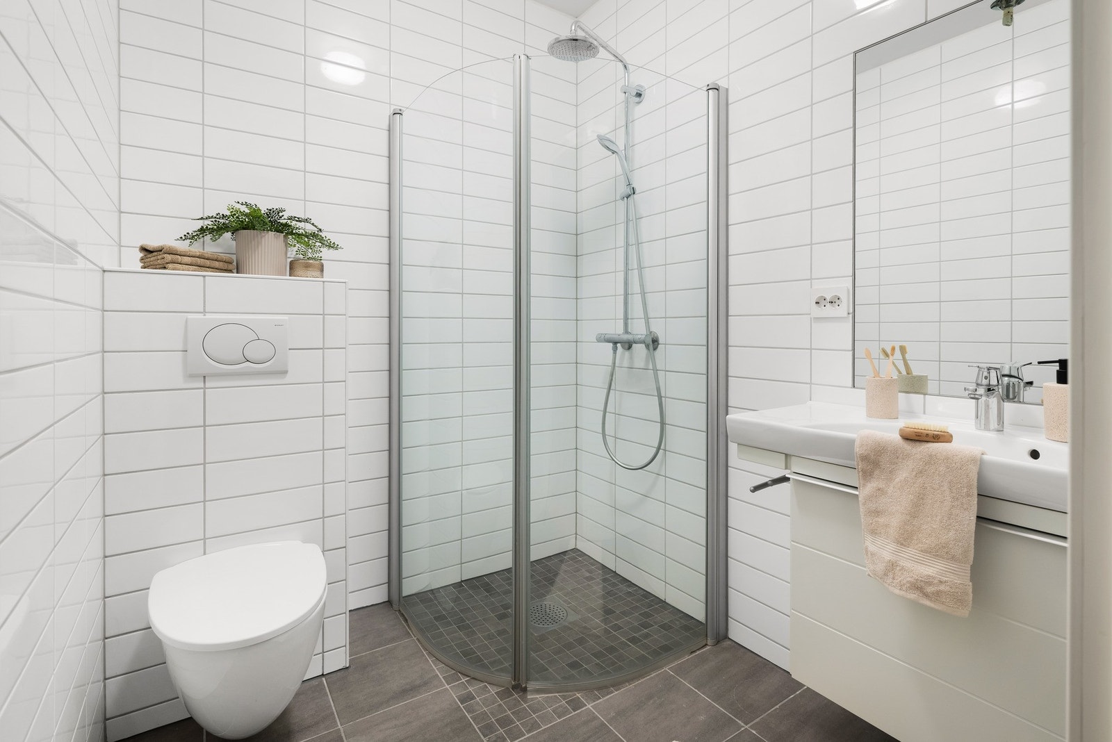 Baderomsinnredningen består av vegghengt toalett, helstøpt servant, skuffer under servant med profilerte fronter, og dusjdører i klart glass. Galleribilde