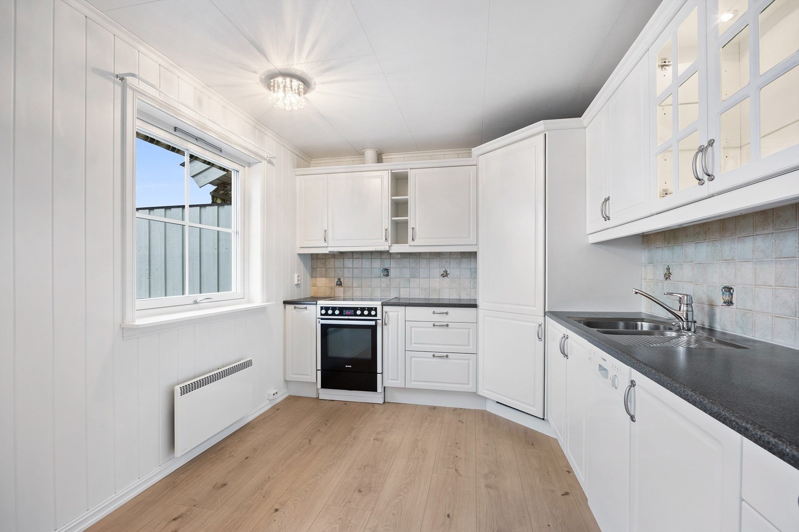 Innredningen har hvite, profilerte fronter, vitrinedører og koksgrå laminatbenkeplate med planlimt kum. Galleribilde