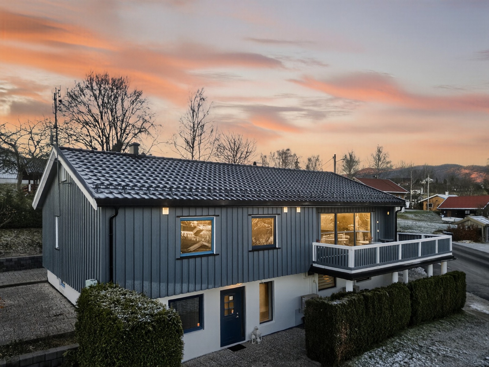 Boligen har en mørk blå fasade med store vinduer og balkong i 2. etasje. Galleribilde