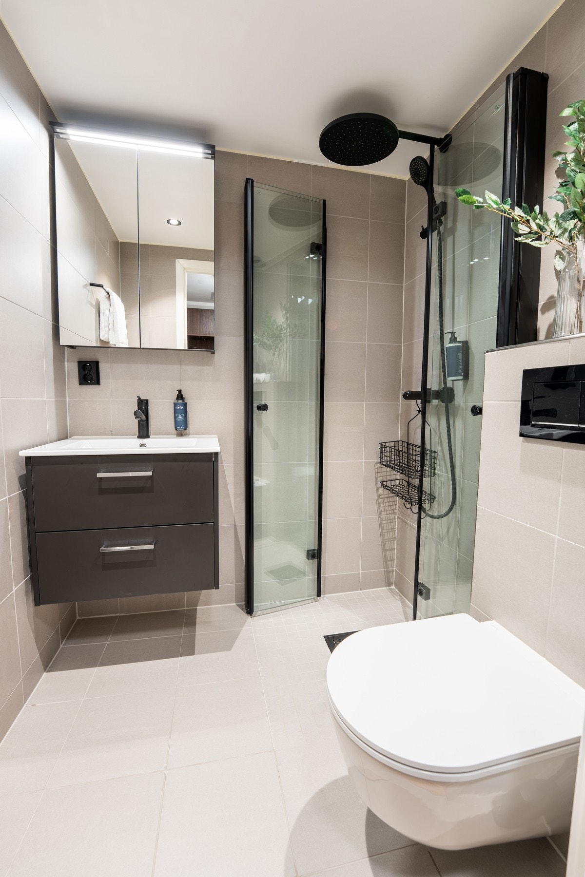 Lekkert bad med delikate fargevalg. Flislagt på gulv og vegger, og innredet med vegghengt toalett, servantinnredning og dusjvegger i glass Galleribilde