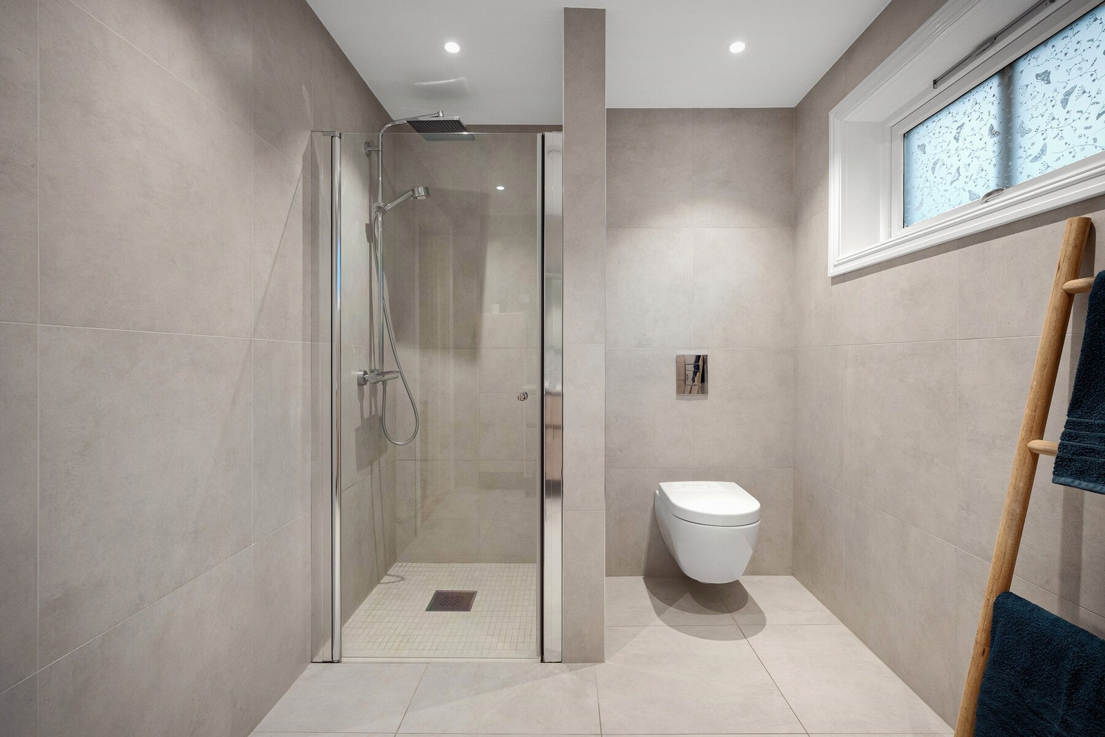 Badet er innredet med vegghengt toalett, servantinnredning med heldekkende servant, speil med belysning og dusjhjørne med glassdører og regnfallsdusj. Galleribilde