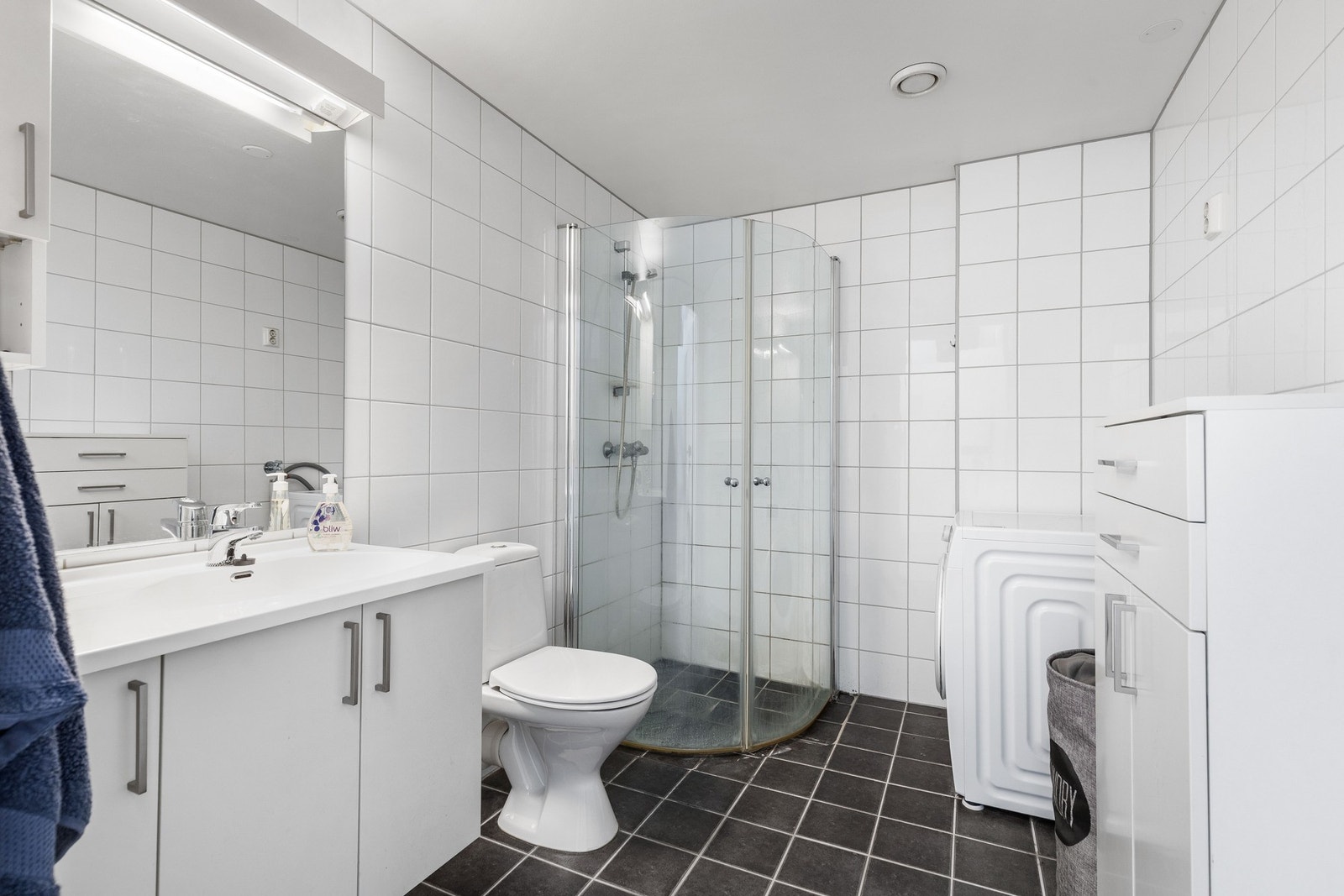 Badet er flislagt og innredet med dusjhjørne, toalett og servant med baderomsinnredning. Galleribilde