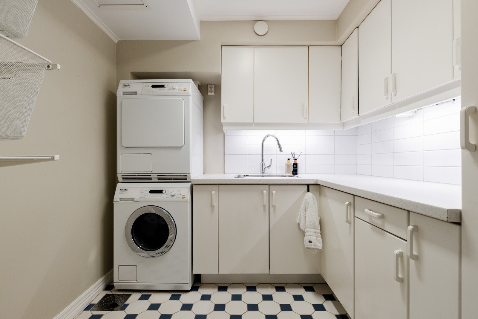 Romslig vaskerom med flislagt gulv og malte overflater. Opplegg for vaskemaskin og tørketrommel. Galleribilde