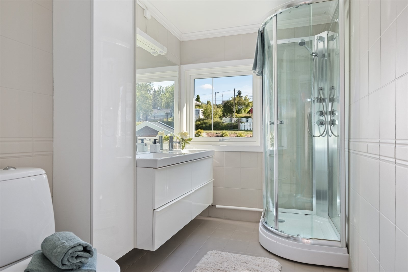 Baderommet i 1. etg. har flis på gulv og vegger, malte plater i himling. Dusjkabinett, innredning med dobbel servant, langskap og toalett. Galleribilde