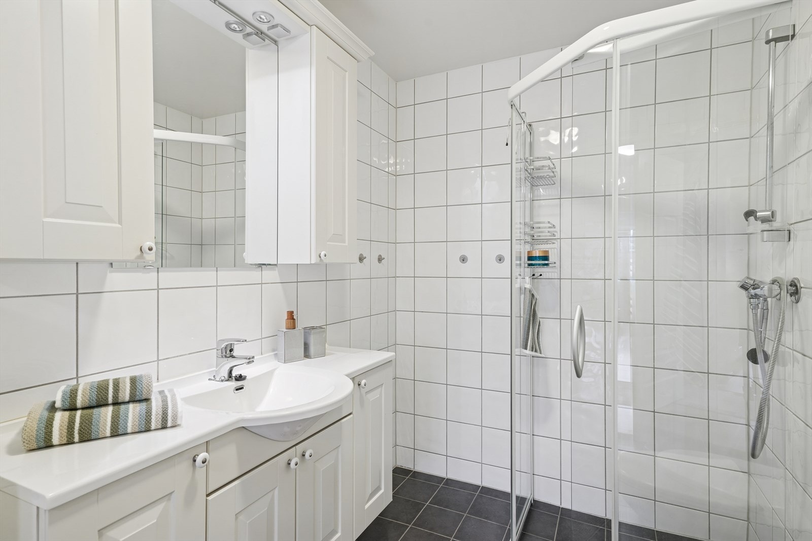 Badet er utstyrt med vegghengt toalett, stor baderomsinnredning med nedfelt servant, vegghengt skap og dusjhjørne med skyvedører av glass. Galleribilde