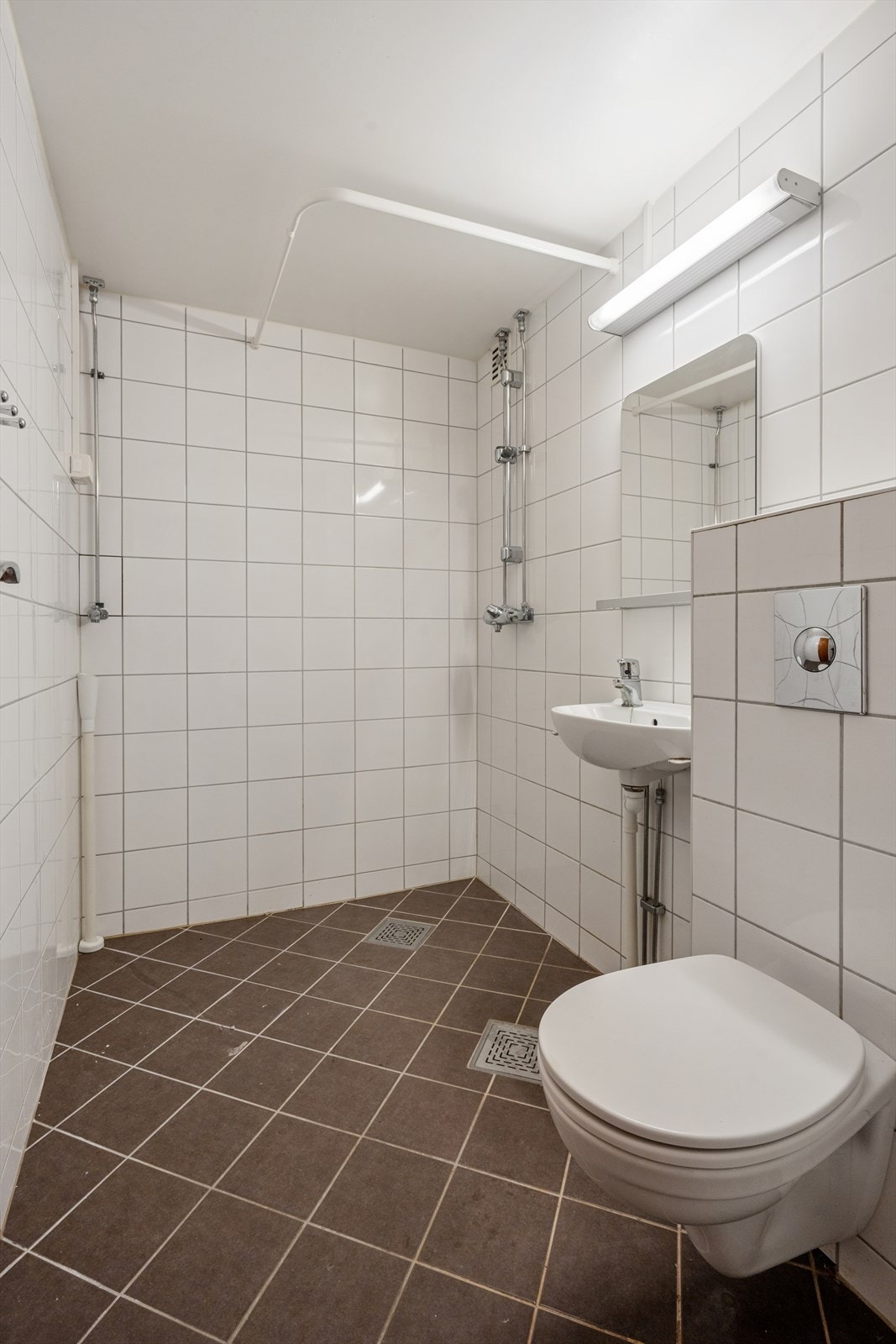 Badet er innredet med vegghengt servant med ett-greps blandebatteri, veggspeil, lysarmatur, vegghengt toalett med innebygget sisterne og blandebatteri. Galleribilde