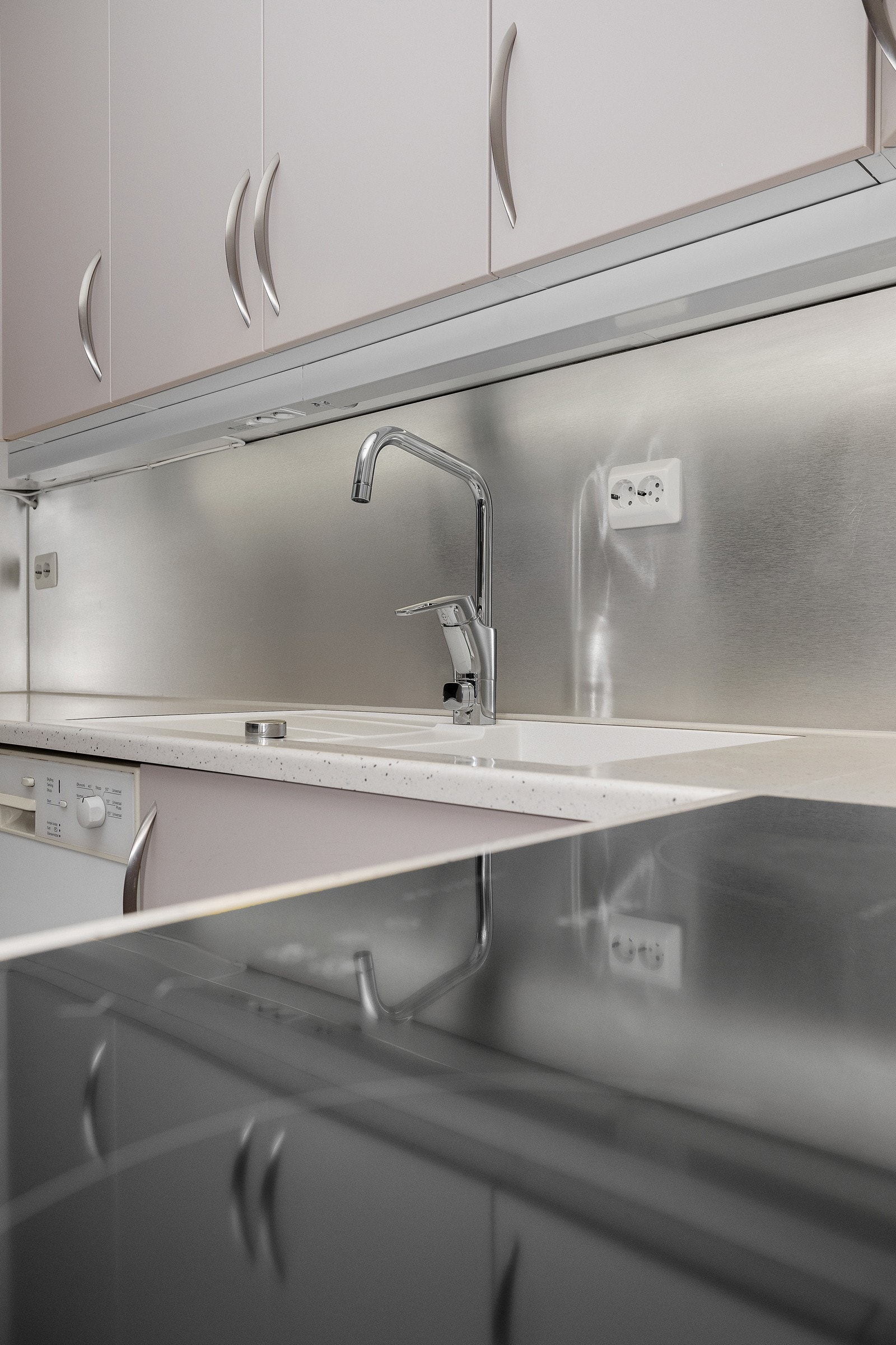 Det er laminat benkeplate og plater i stål (eller lignende) mellom kjøkkenbenk og overskap. Galleribilde